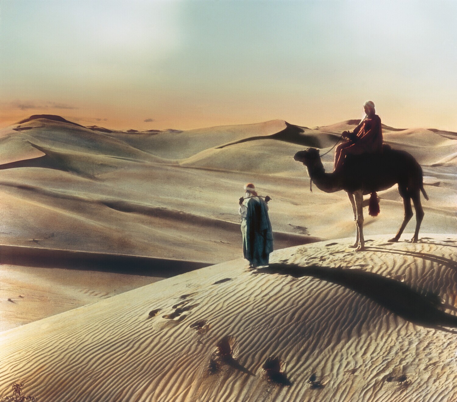 Historisches, handkoloriertes Foto von zwei Nomaden mit Kamel in der Wüste bei Sonnenuntergang