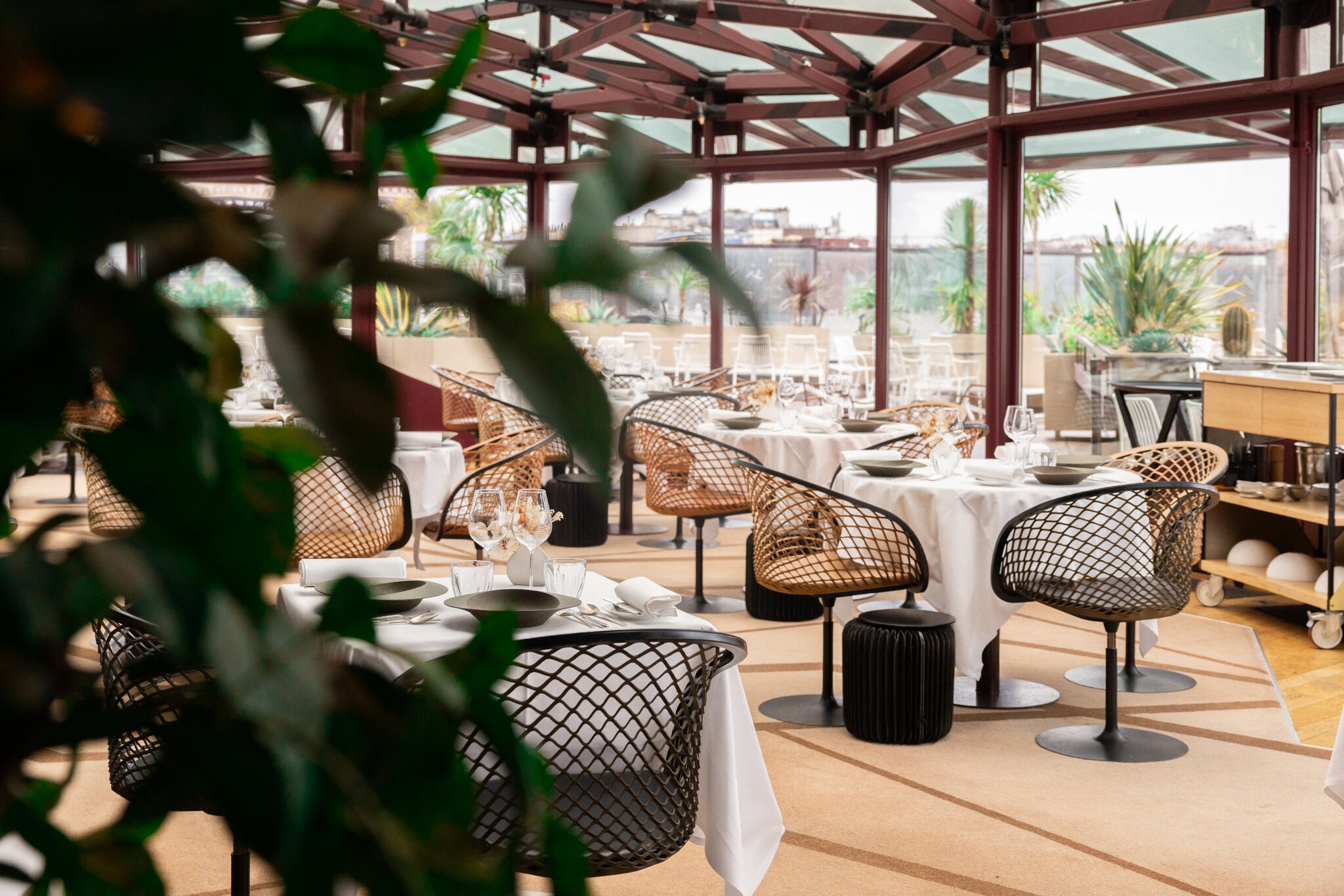 Interieur-Aufnahme eines modernen Restaurants mit gedeckten Tischen und bodentiefen Fenstern, die den Blick auf Paris freigeben.