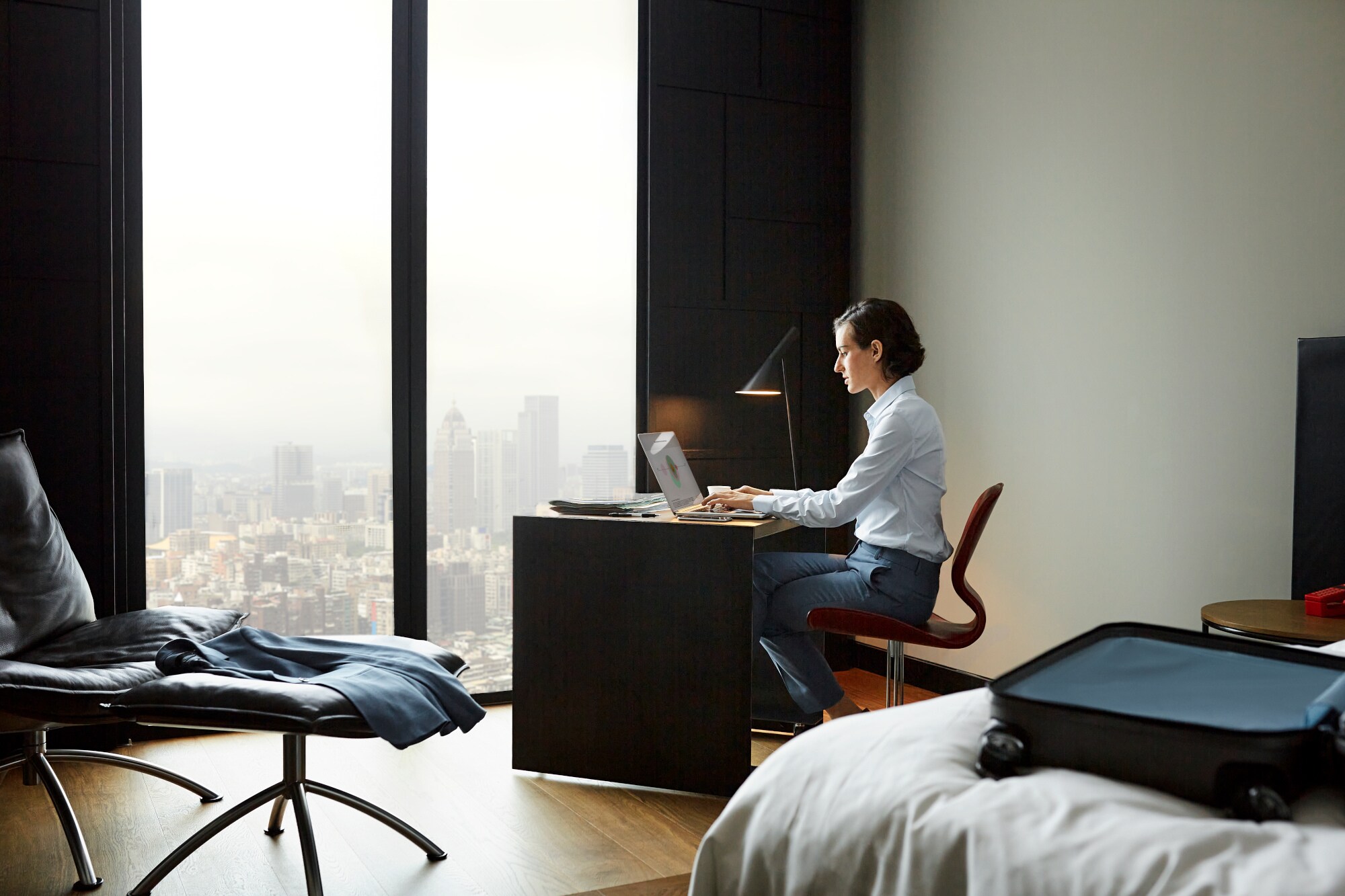 Eine Geschäftsfrau arbeitet in einem Hotelzimmer an einem Schreibtisch an ihrem Laptop Eine Geschäftsfrau arbeitet in einem Hotelzimmer an einem Schreibtisch an ihrem Laptop