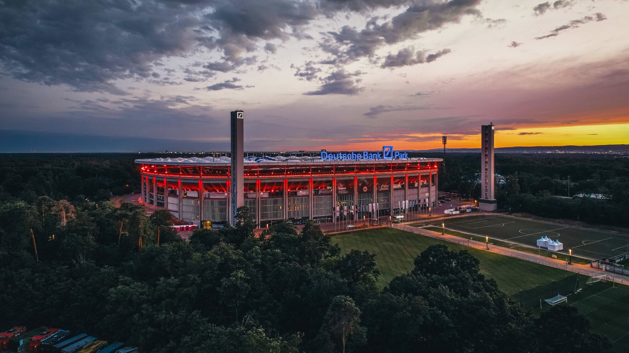 Rot beleuchtetes Stadion mit Deutsche-Bank-Logo in einem Waldgebiet bei Dunkelheit.
