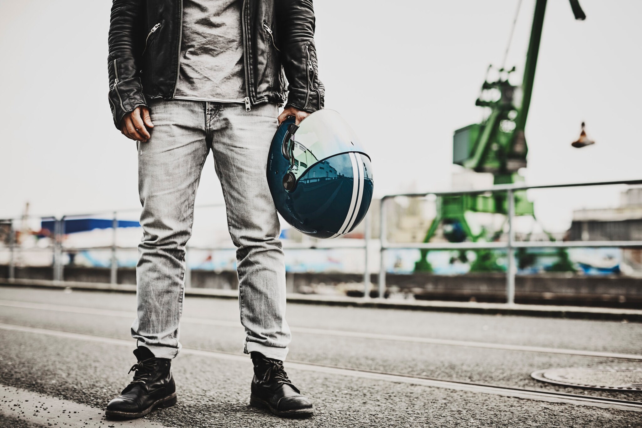 Unterkörper eines Mannes in lässiger Kleidung in einem Industriegebiet, der in einer Hand einen blauen Motorradhelm trägt