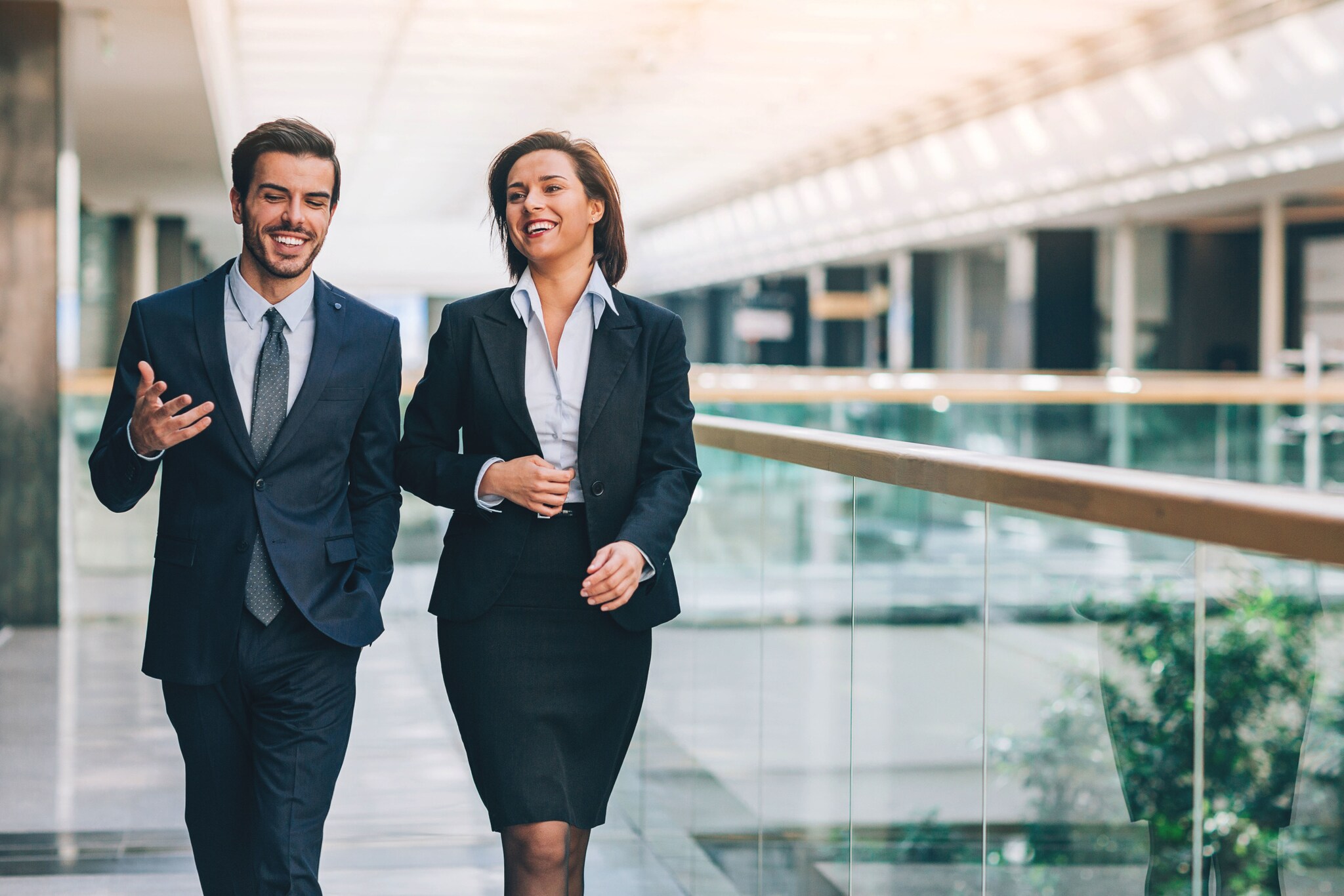 Ein Mann und eine Frau in formeller Business-Kleidung kommunizieren nebeneinander gehend.
