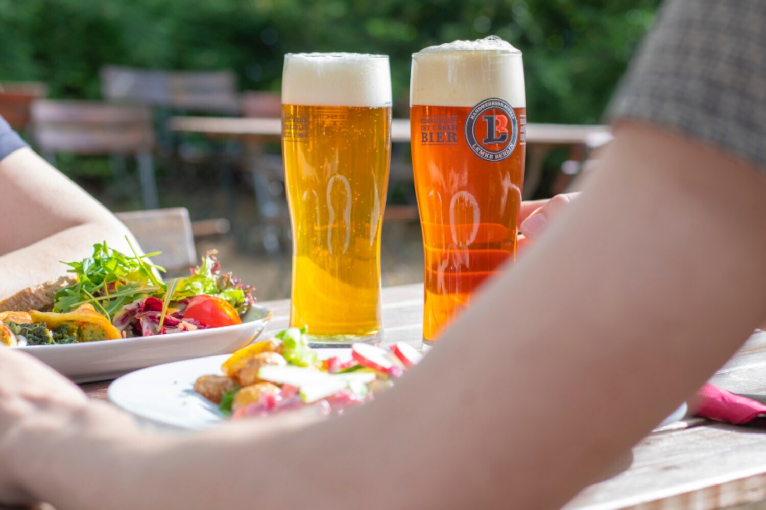 Zwei Gläser mit Bier und zwei gefüllte Teller mit Salat auf einem Tisch