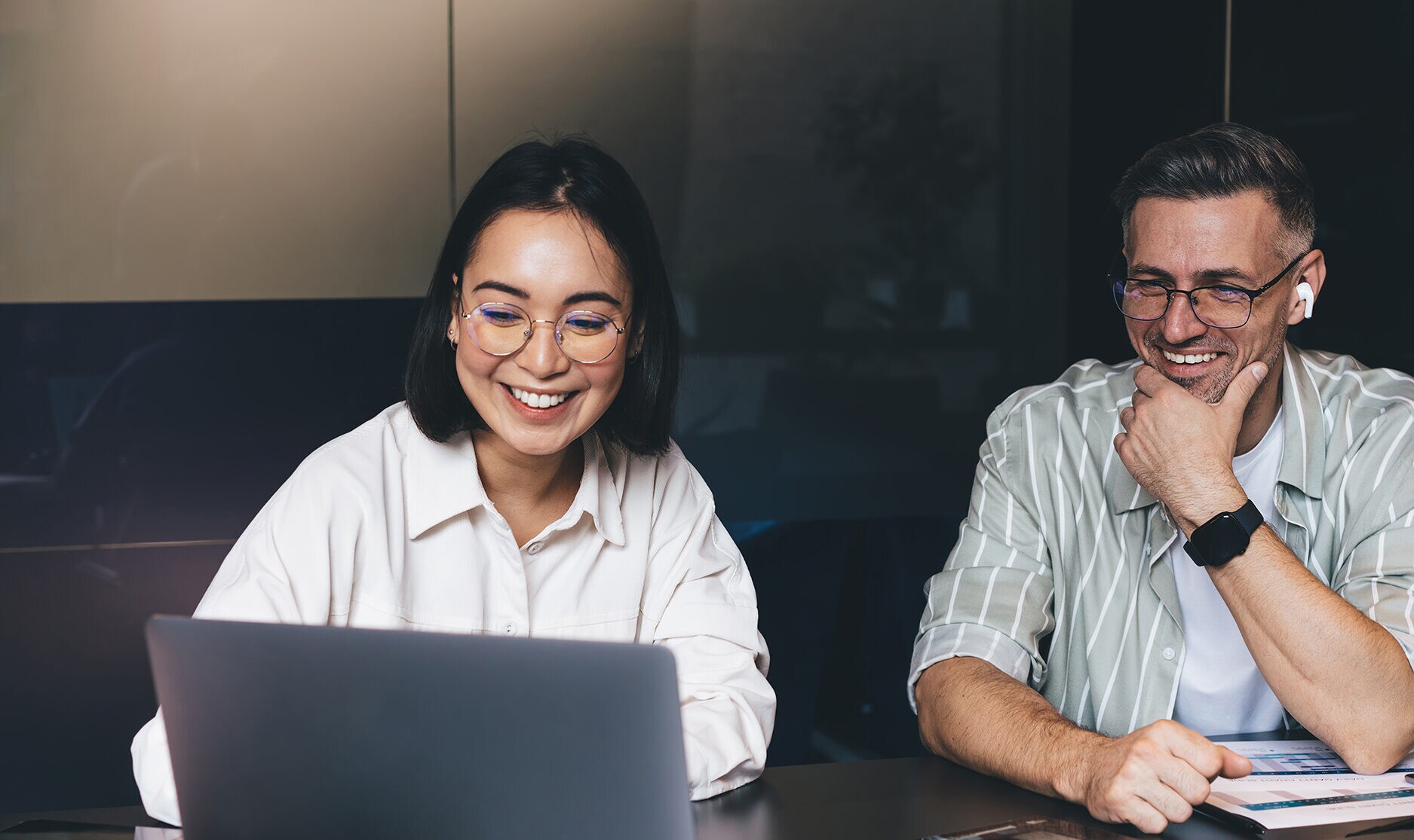 Soft Skills, die zählen: Stärke dein Business & dein Team Zwei Kolleg:innen schauen zusammen auf einen Laptop und freuen sich.