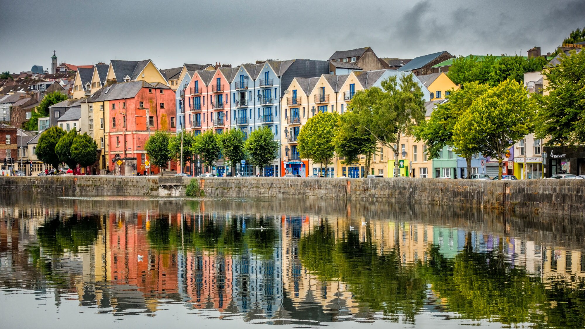 Bunte Wohngebäude in verschiedenen Farben spiegeln sich im ruhigen Wasser eines Hafens. Bäume stehen entlang der Uferpromenade. Bunte Wohngebäude in verschiedenen Farben spiegeln sich im ruhigen Wasser eines Hafens. Bäume stehen entlang der Uferpromenade.