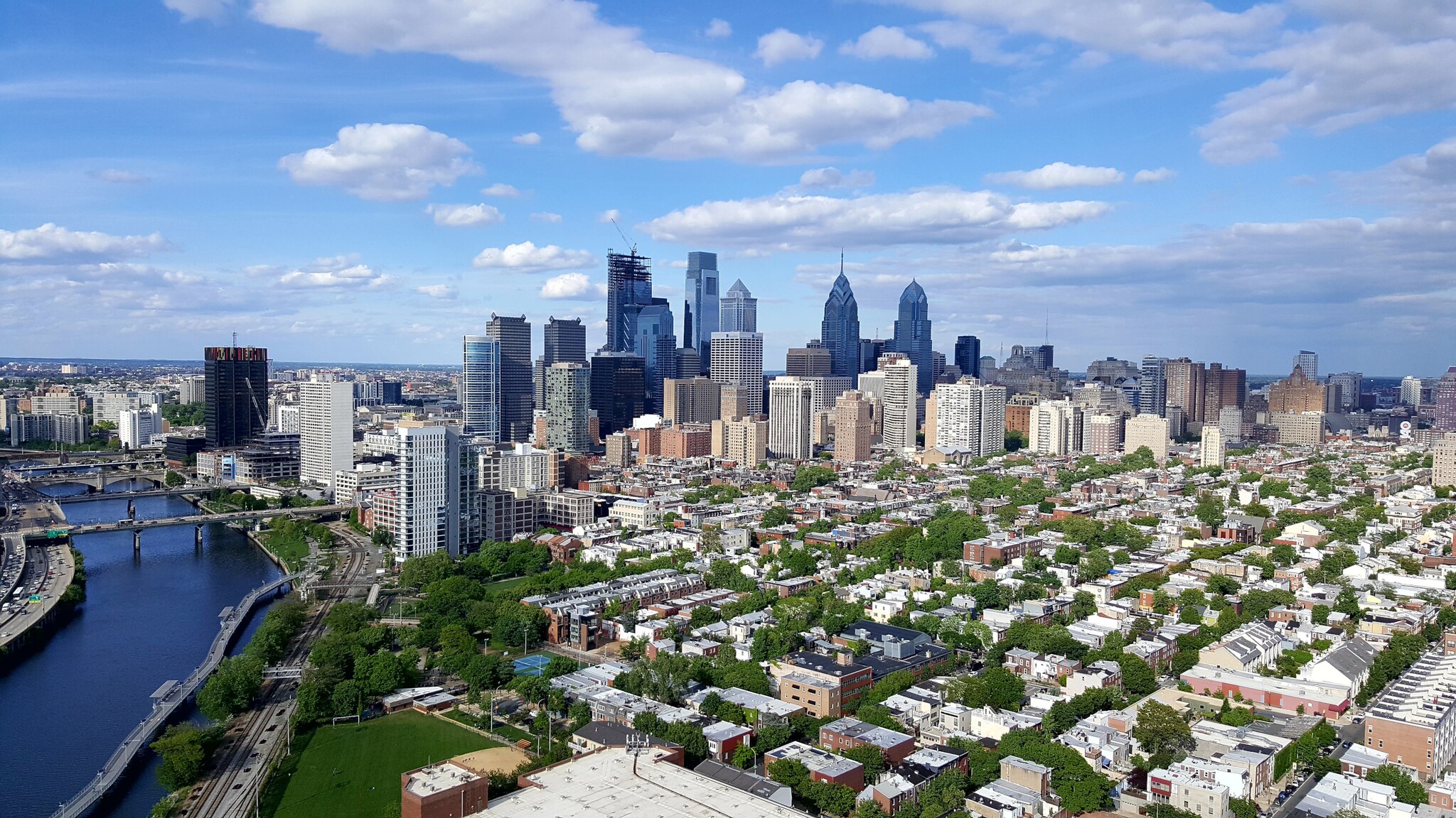 Skyline von Philadelphia mit niedrigen Häusern in begrüntem Wohnviertel vor Hochhäusern im Hintergrund.