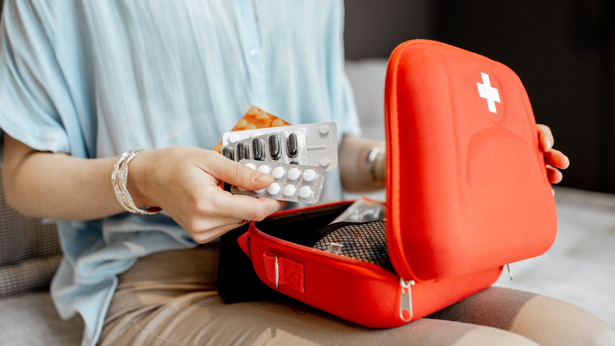 Person hält Tablettenblister über einem roten Erste-Hilfe-Set mit weißem Kreuz.