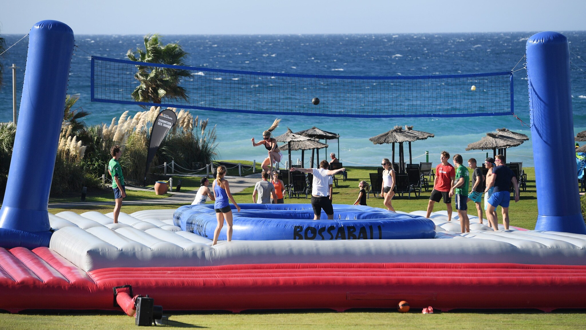 Personen beim Ballspiel an einem Volleyballnetz auf einer Hüpfburg am Meer.