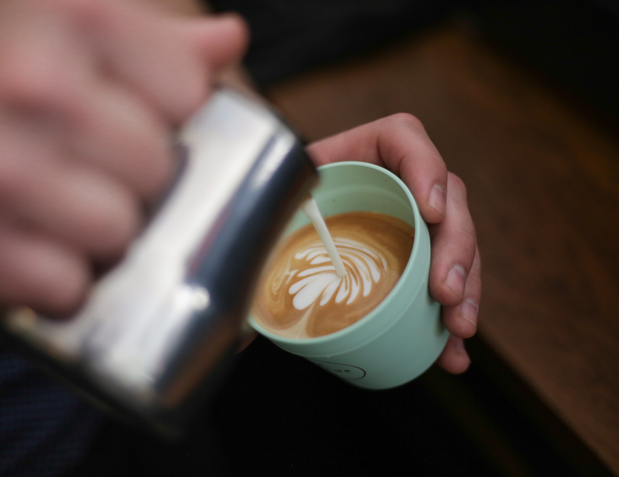Eine Hand gießt aufgeschäumte Milch in einen Plastikbecher mit Kaffee Eine Hand gießt aufgeschäumte Milch in einen Plastikbecher mit Kaffee