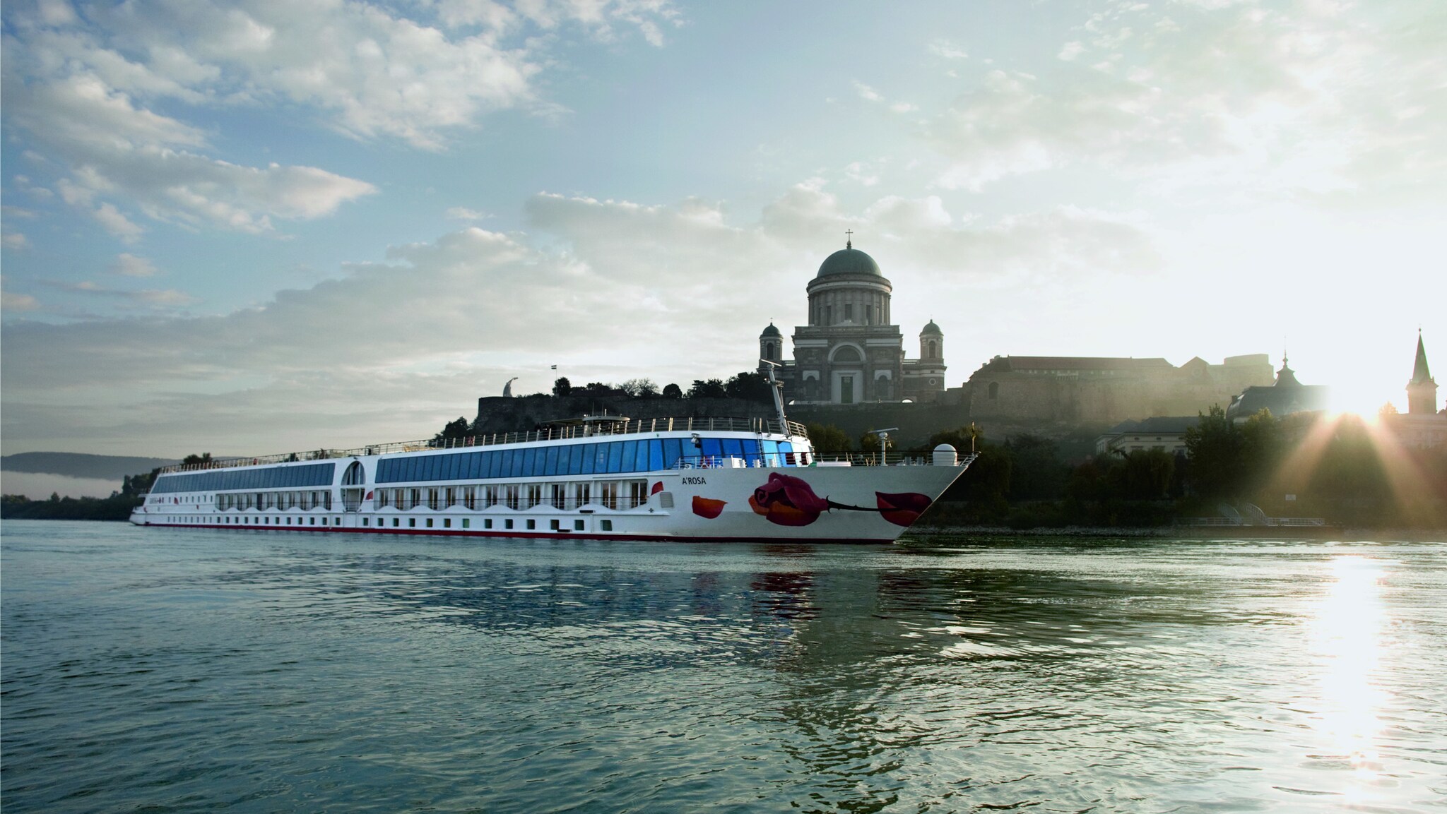 Ein Kreuzfahrtschiff von A-ROSA auf einem Fluss vor dem Panorama einer Stadt mit Kirche.