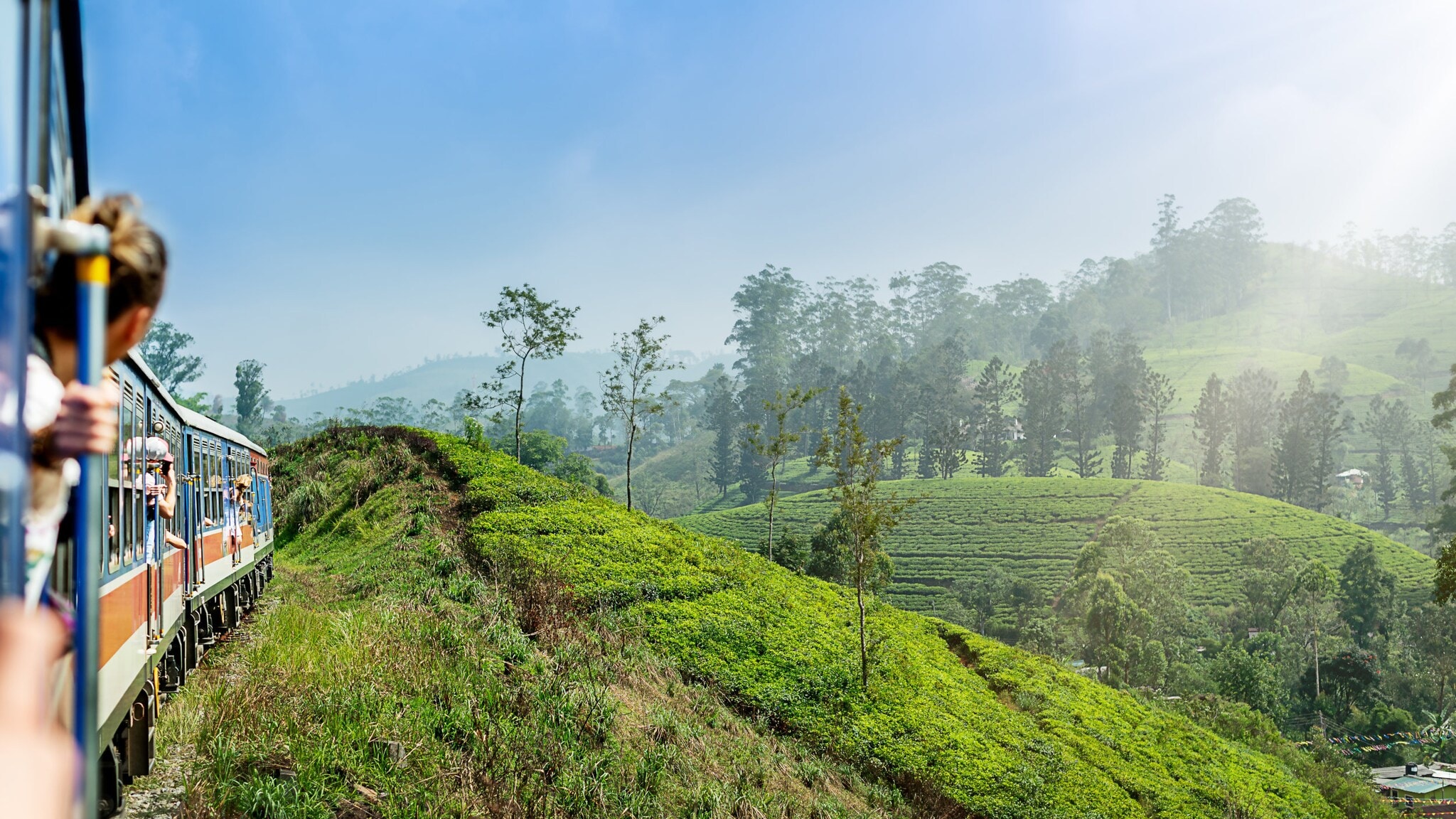 Ein Zug fährt entlang einer grünen Hügelkette, umgeben von Bäumen und Pflanzen. Im Vordergrund ist eine Hand zu sehen, die den Zug hält. Ein Zug fährt entlang einer grünen Hügelkette, umgeben von Bäumen und Pflanzen. Im Vordergrund ist eine Hand zu sehen, die den Zug hält.