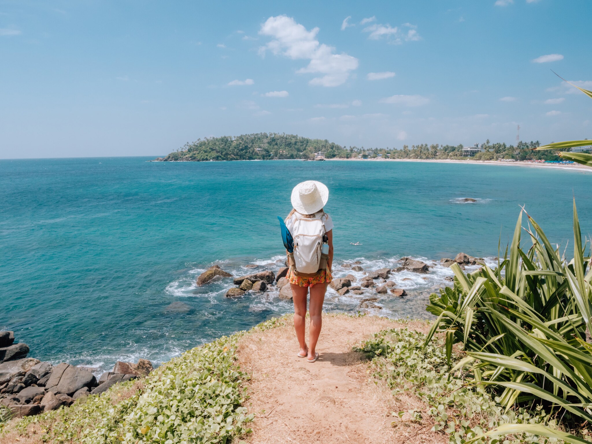 Eine Person mit Sonnenhut steht auf einer Klippe Richtung Meer, vor ihr die Küstenlandschaft Sri Lankas. Eine Person mit Sonnenhut steht auf einer Klippe Richtung Meer, vor ihr die Küstenlandschaft Sri Lankas.