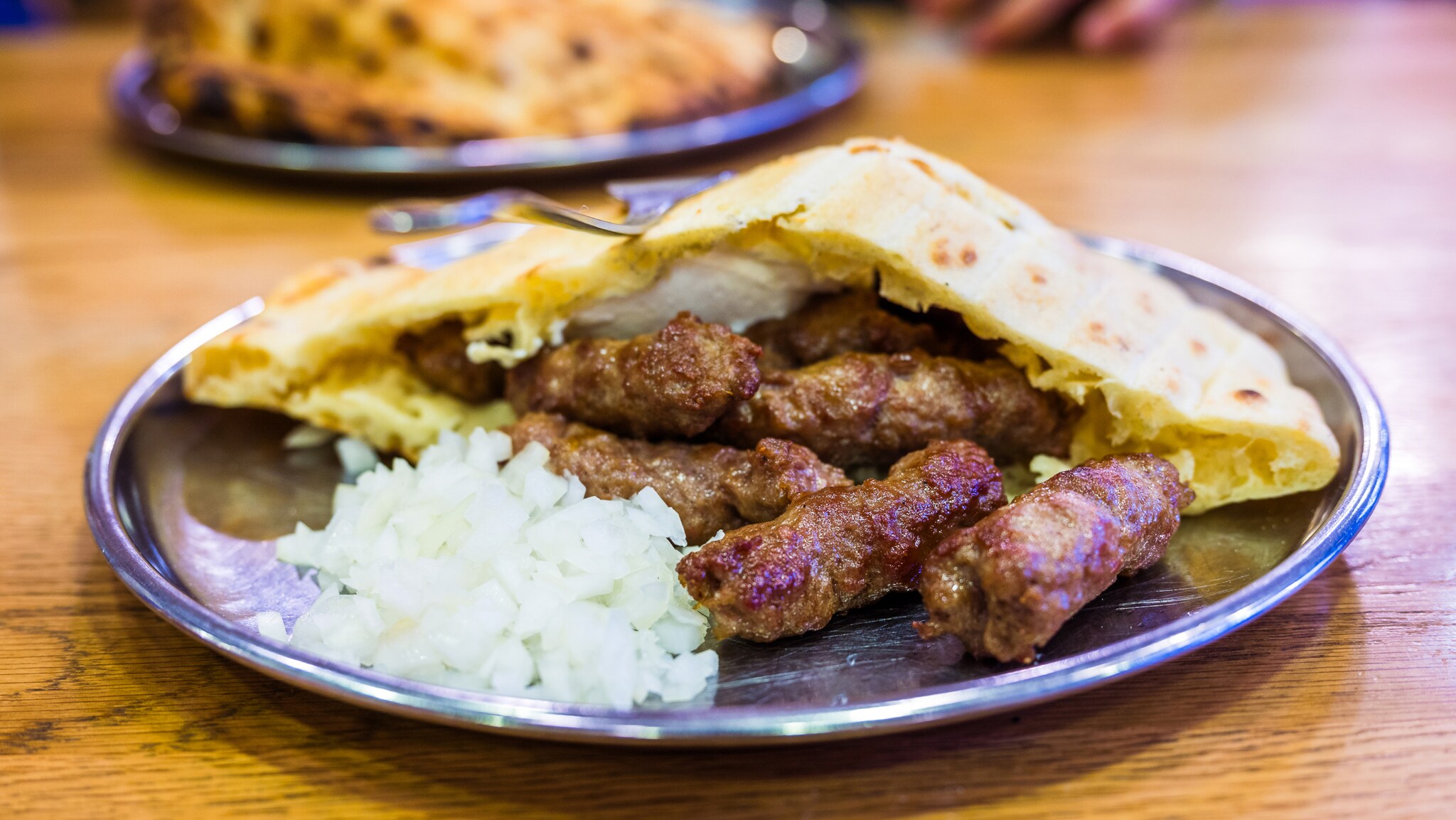Metallteller mit mehreren gegrillten Cevapcici, gehackten Zwiebeln und Fladenbrot auf Holztisch. Metallteller mit mehreren gegrillten Cevapcici, gehackten Zwiebeln und Fladenbrot auf Holztisch.