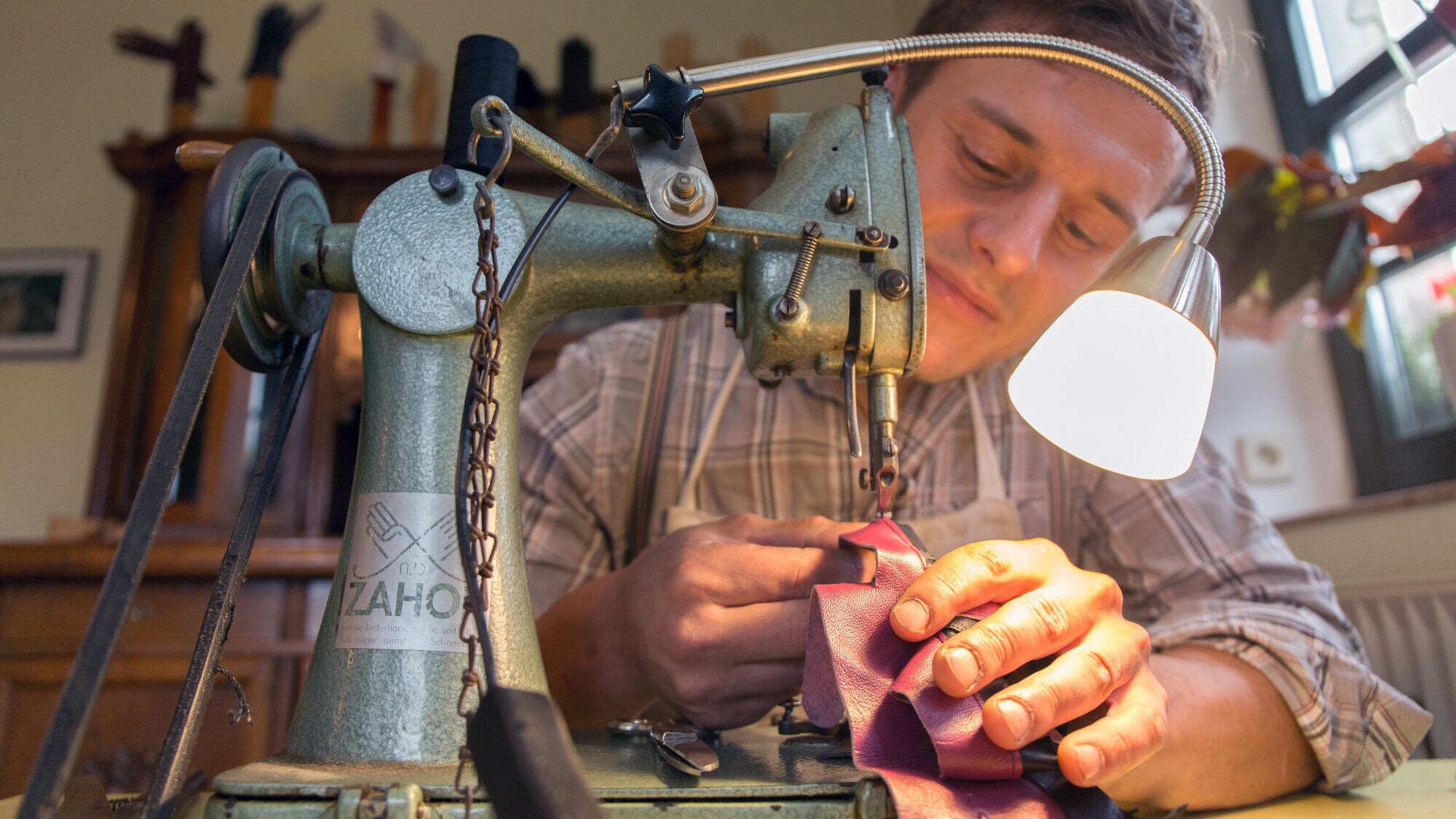 Nahaufnahme eines Mannes hinter einer antiken Nähmaschine bei der Anfertigung eines Lederhandschuhs in einem Atelier. Nahaufnahme eines Mannes hinter einer antiken Nähmaschine bei der Anfertigung eines Lederhandschuhs in einem Atelier.