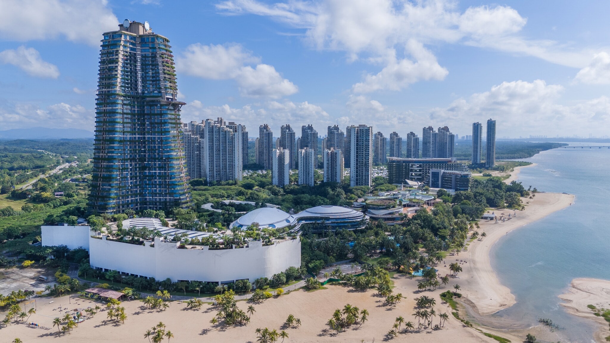 Blick auf eine moderne Küstenstadt in Ägypten mit hohem, runder Turm im Bau, mehreren Hochhäusern und einem Sandstrand am Meer. Blick auf eine moderne Küstenstadt in Ägypten mit hohem, runder Turm im Bau, mehreren Hochhäusern und einem Sandstrand am Meer.