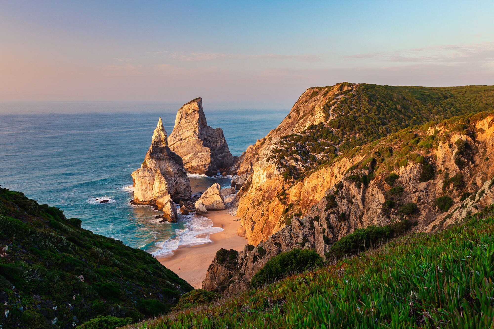 Der einsame Praia da Ursa mit seinen markanten Felsformationen von den Klippen aus und bei leichter Dämmerung in goldenem Licht.