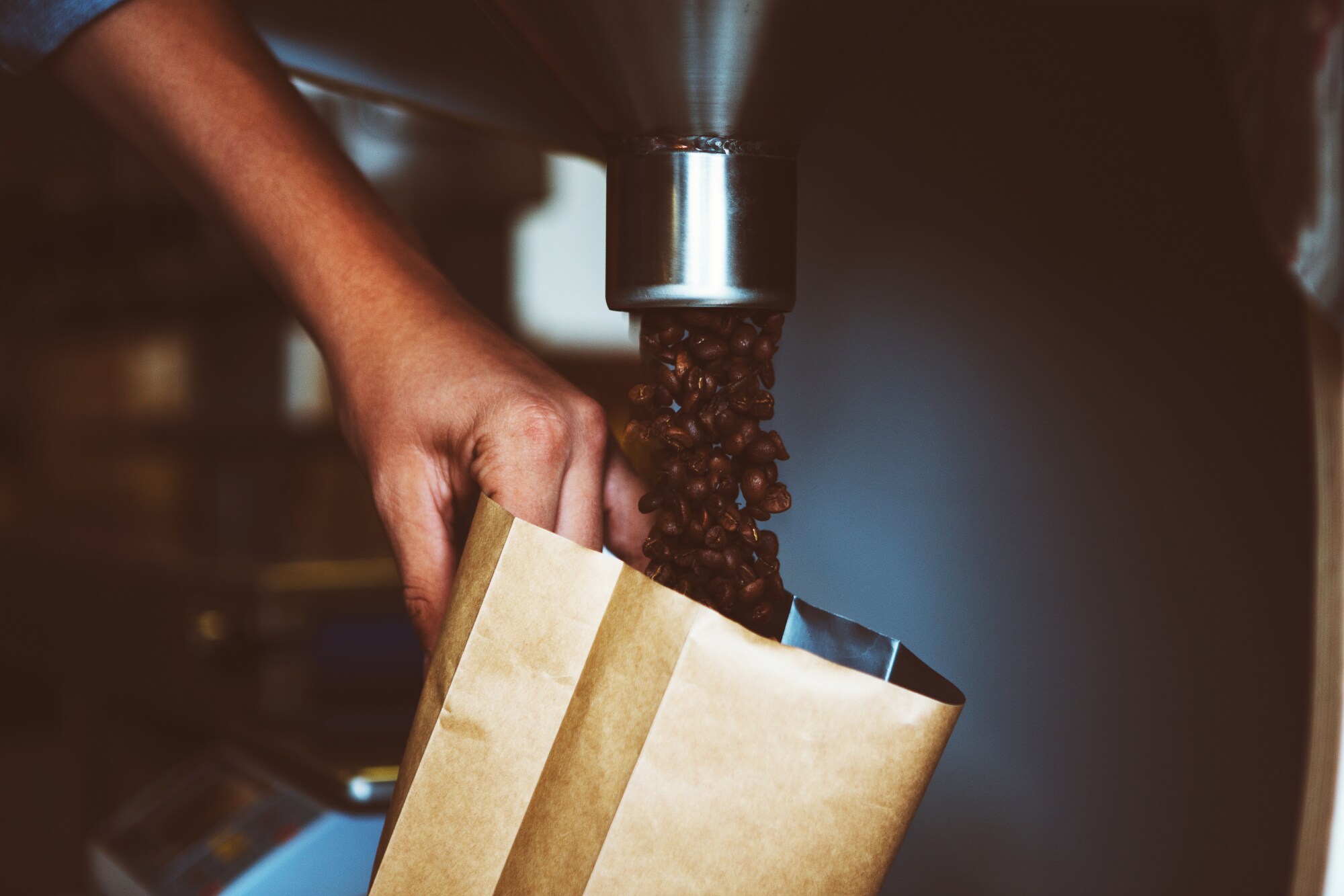 Nahaufnahme einer Hand, die Kaffeebohnen in eine Verpackung abfüllt