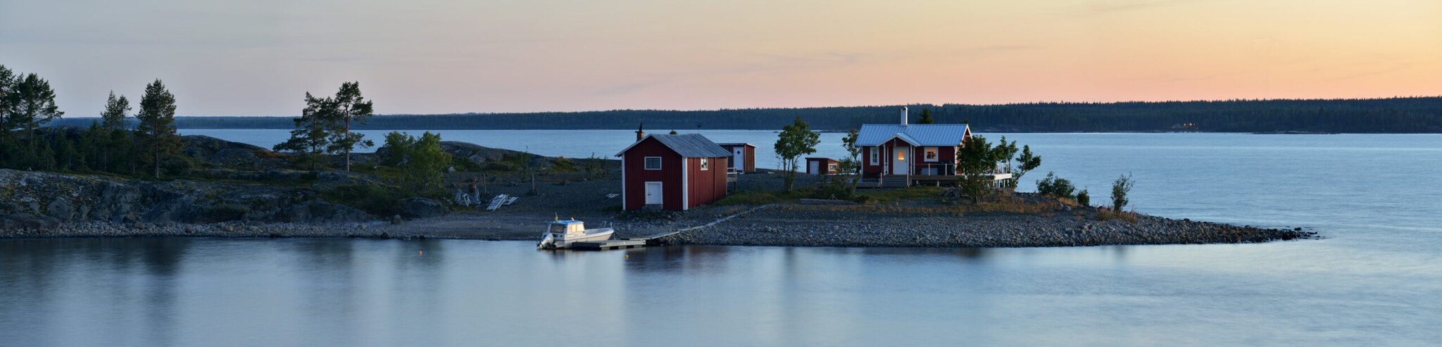 Eine schwedische Insel mit einem roten Holzhaus mit Bootsanleger in der Dämmerung