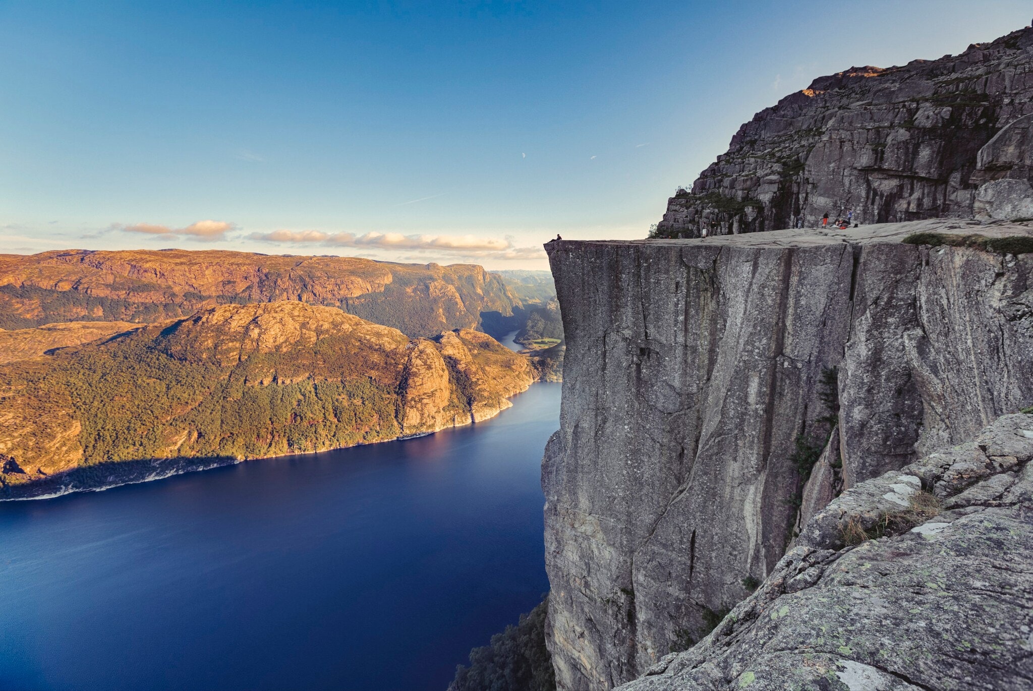 Fjordlandschaft an einem klaren Tag mit Personen auf einer beeindruckenden Felsklippe. Fjordlandschaft an einem klaren Tag mit Personen auf einer beeindruckenden Felsklippe.