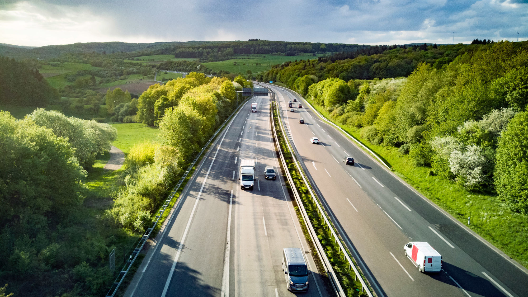 Autos auf einer mehrspurigen Autobahn in grüner Hügellandschaft bei Sonnenschein aus der Luftperspektive. Autos auf einer mehrspurigen Autobahn in grüner Hügellandschaft bei Sonnenschein aus der Luftperspektive.