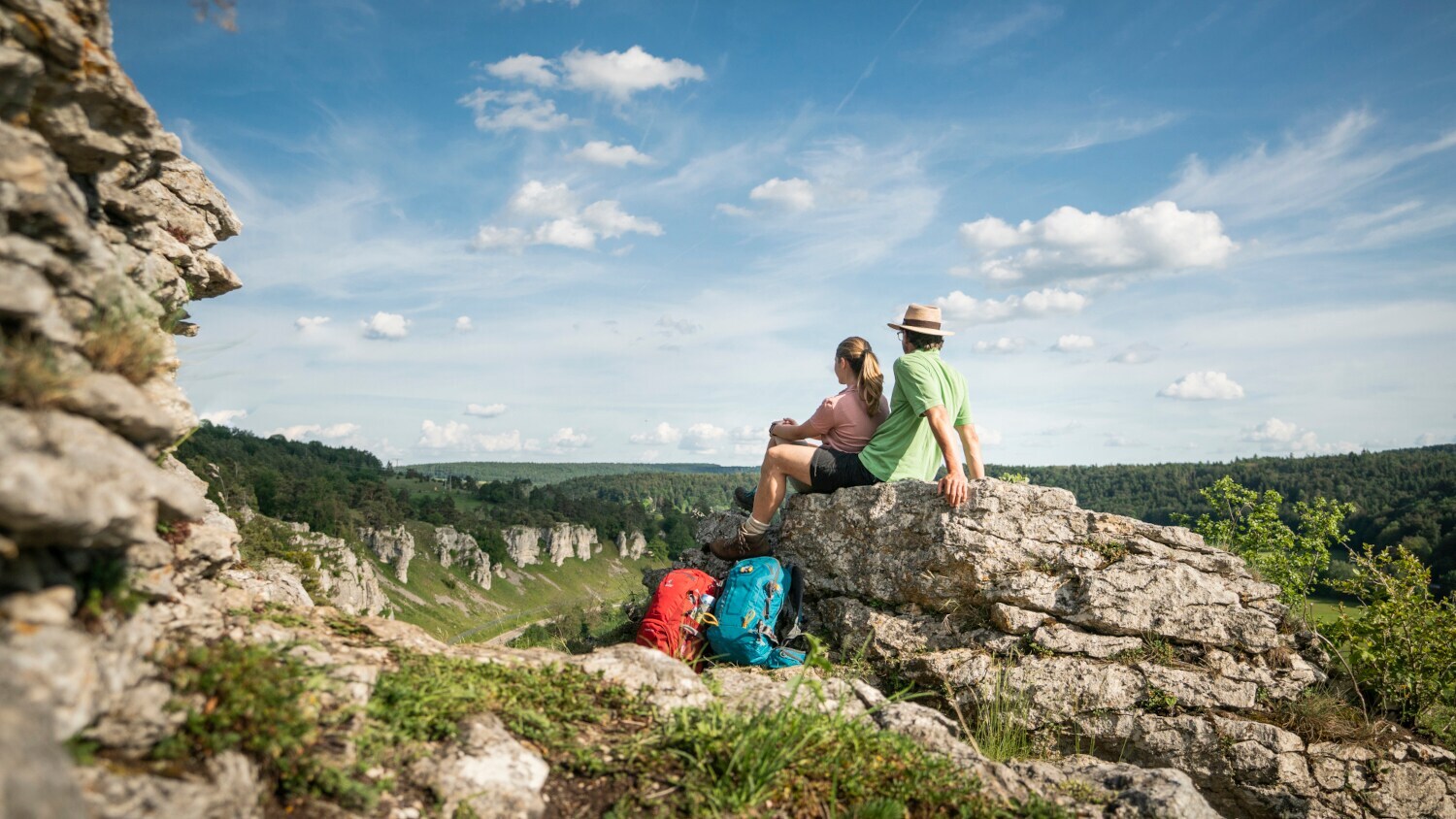 Zwei Wandernde sitzen auf einem Felsen im Altmühltal und blicken auf die Felsformation Zwölf Apostel