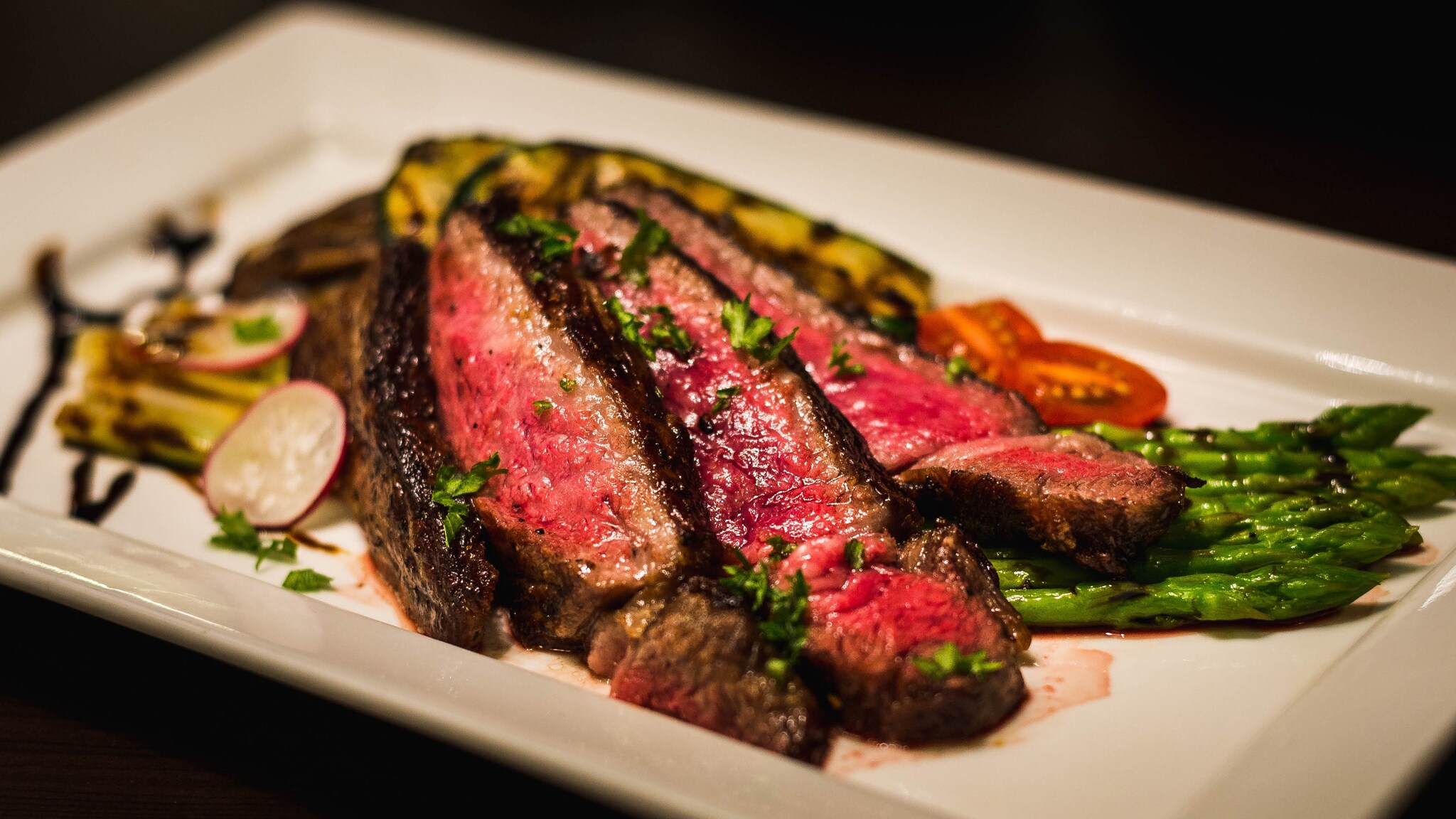 Drei Scheiben rosa gebratenes Rindersteak auf weißem Teller mit gegrilltem Gemüse, Spargel und Radieschenscheiben, garniert mit Kräutern Drei Scheiben rosa gebratenes Rindersteak auf weißem Teller mit gegrilltem Gemüse, Spargel und Radieschenscheiben, garniert mit Kräutern