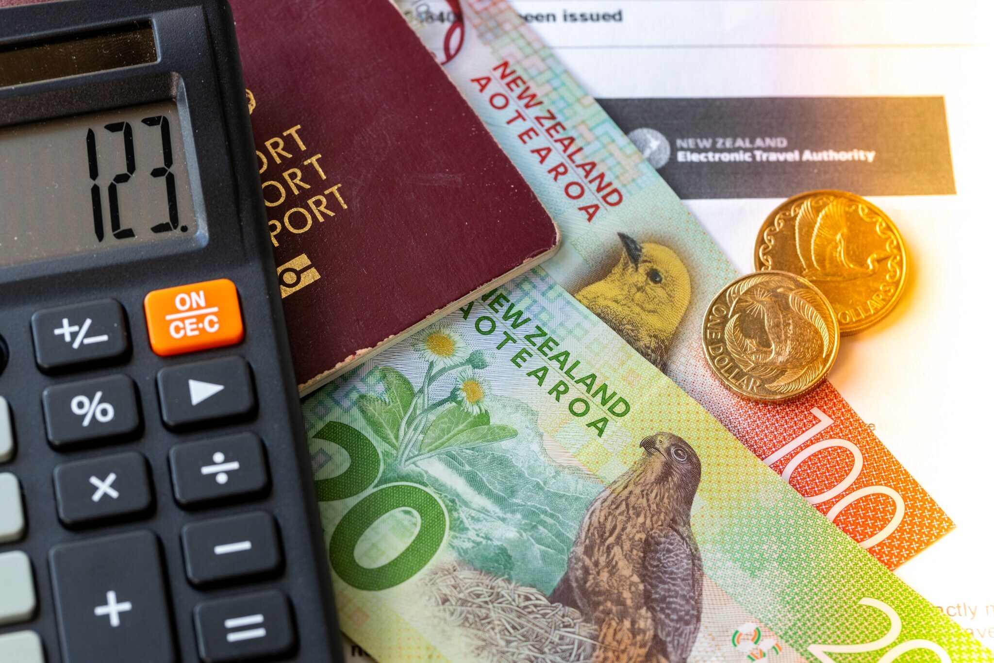 Close-up des NZeTA-Formulars, auf dem neuseeländisches Geld, ein Reisepass sowie ein Taschenrechner liegen.