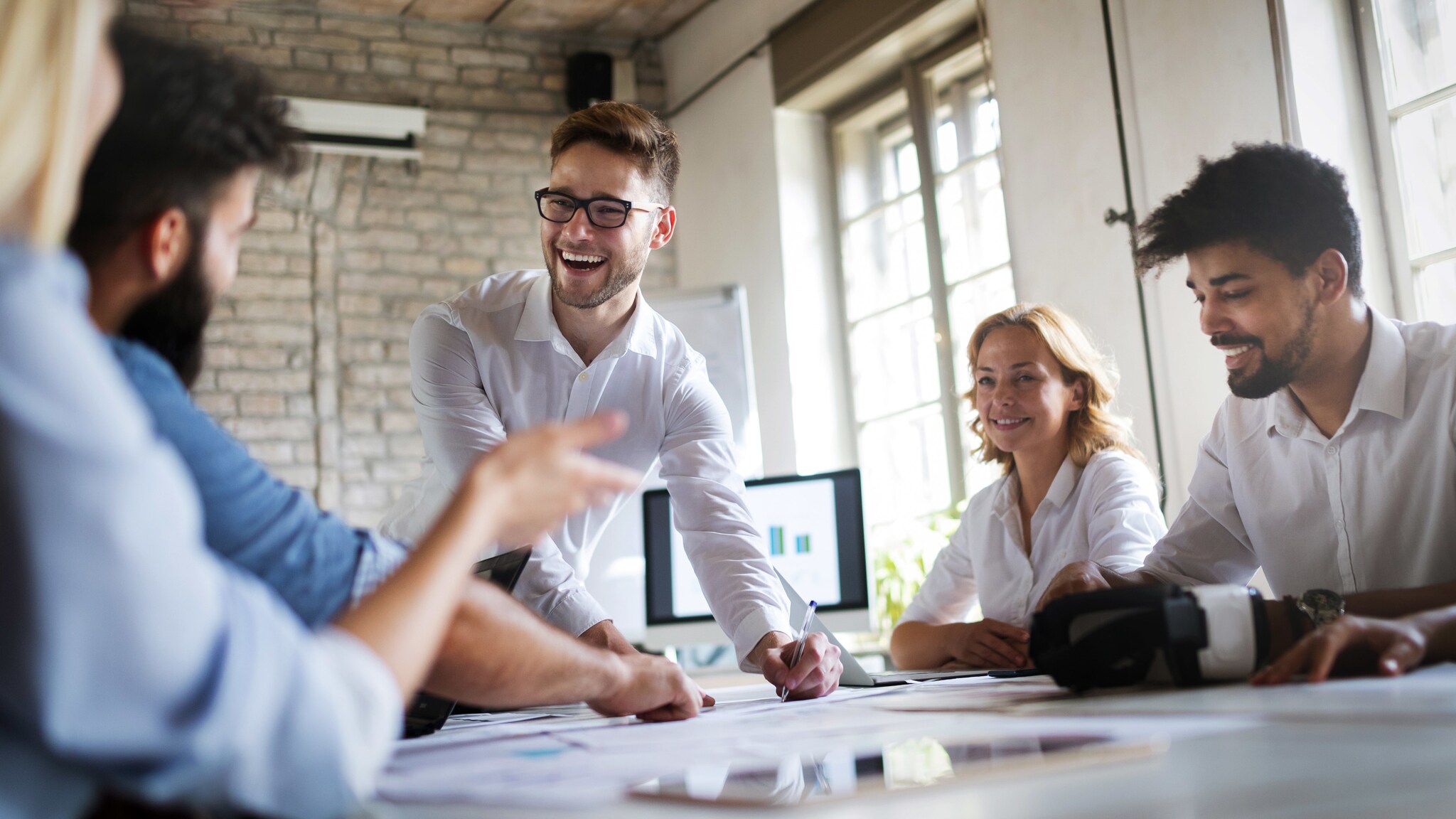 Mehrere lächelnde Personen in Business-Kleidung an einem Tisch mit Arbeitsmaterialien in einem hellen Raum. Mehrere lächelnde Personen in Business-Kleidung an einem Tisch mit Arbeitsmaterialien in einem hellen Raum.