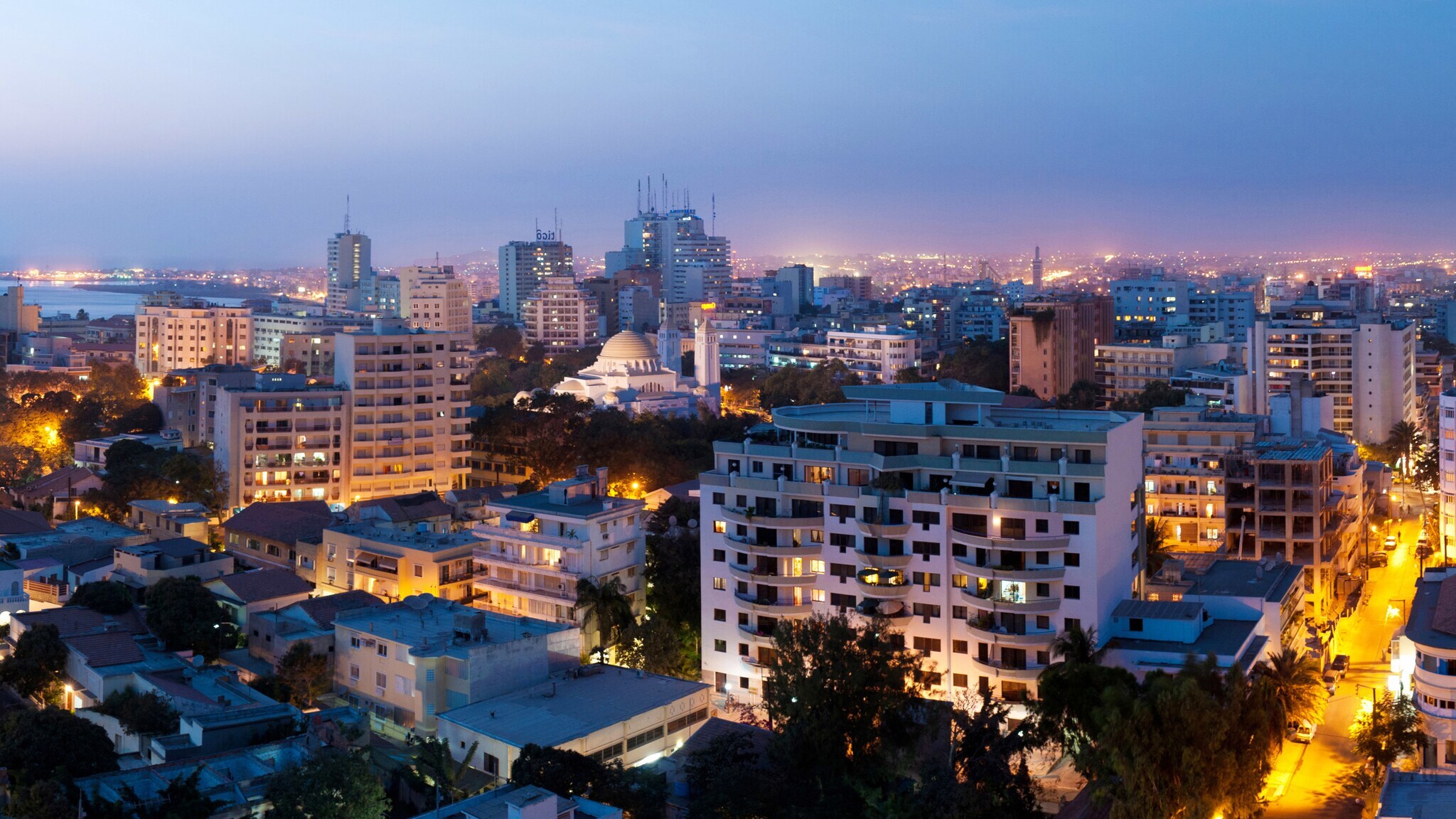 Erleuchtete Skyline von Dakar mit Hochhäusern und Moschee bei Nacht.