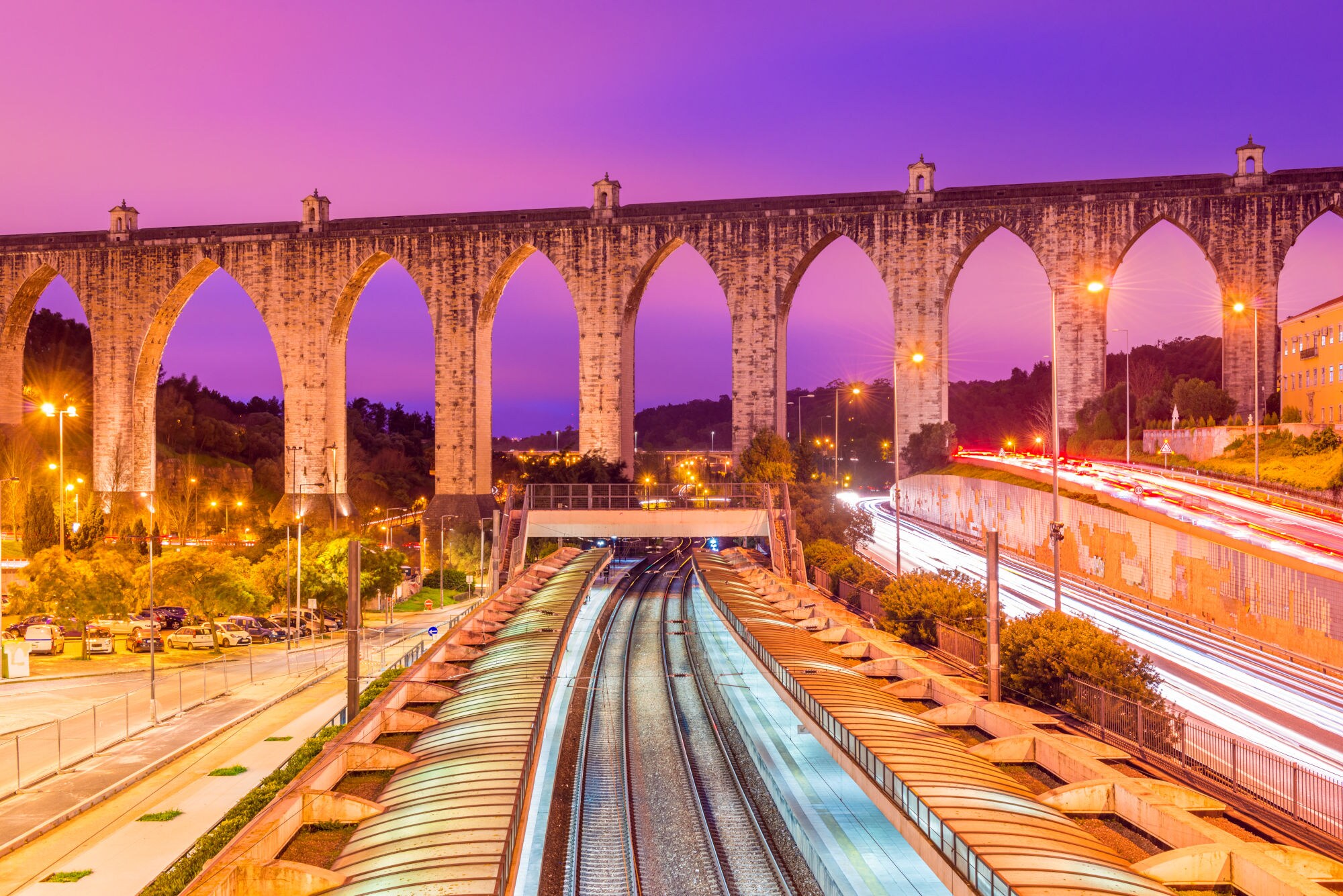 Blick auf das historische Aqueduto das Águas Livres am Bahnhof Campolide am Abend mit einem surreal wirkenden Himmel im Lilatönen. Blick auf das historische Aqueduto das Águas Livres am Bahnhof Campolide am Abend mit einem surreal wirkenden Himmel im Lilatönen.