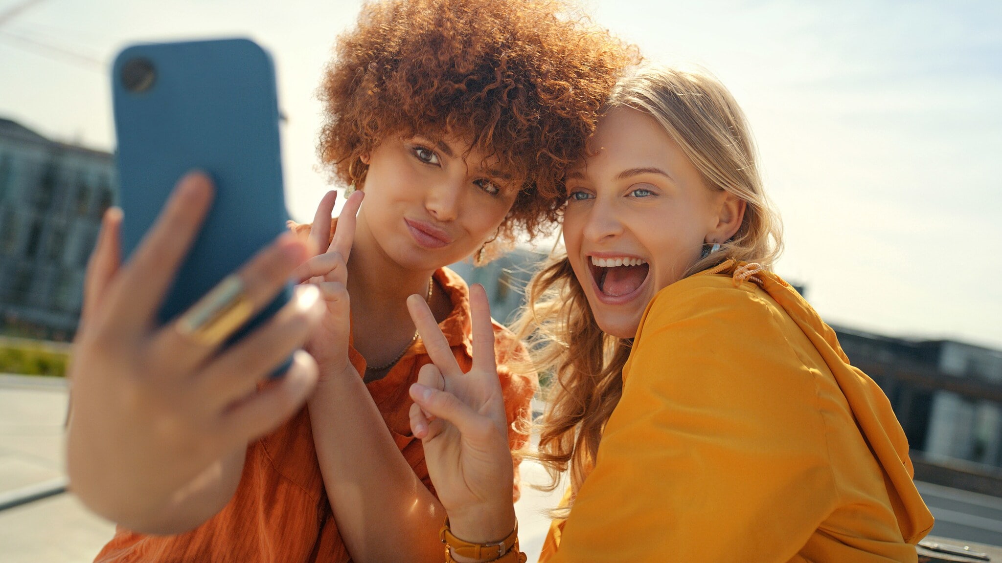 Zwei junge Frauen zeigen Peace-Zeichen mit ihren Fingen, während sie ein Selfie per Smartphone aufnehmen unter freiem Himmel. Zwei junge Frauen zeigen Peace-Zeichen mit ihren Fingen, während sie ein Selfie per Smartphone aufnehmen unter freiem Himmel.