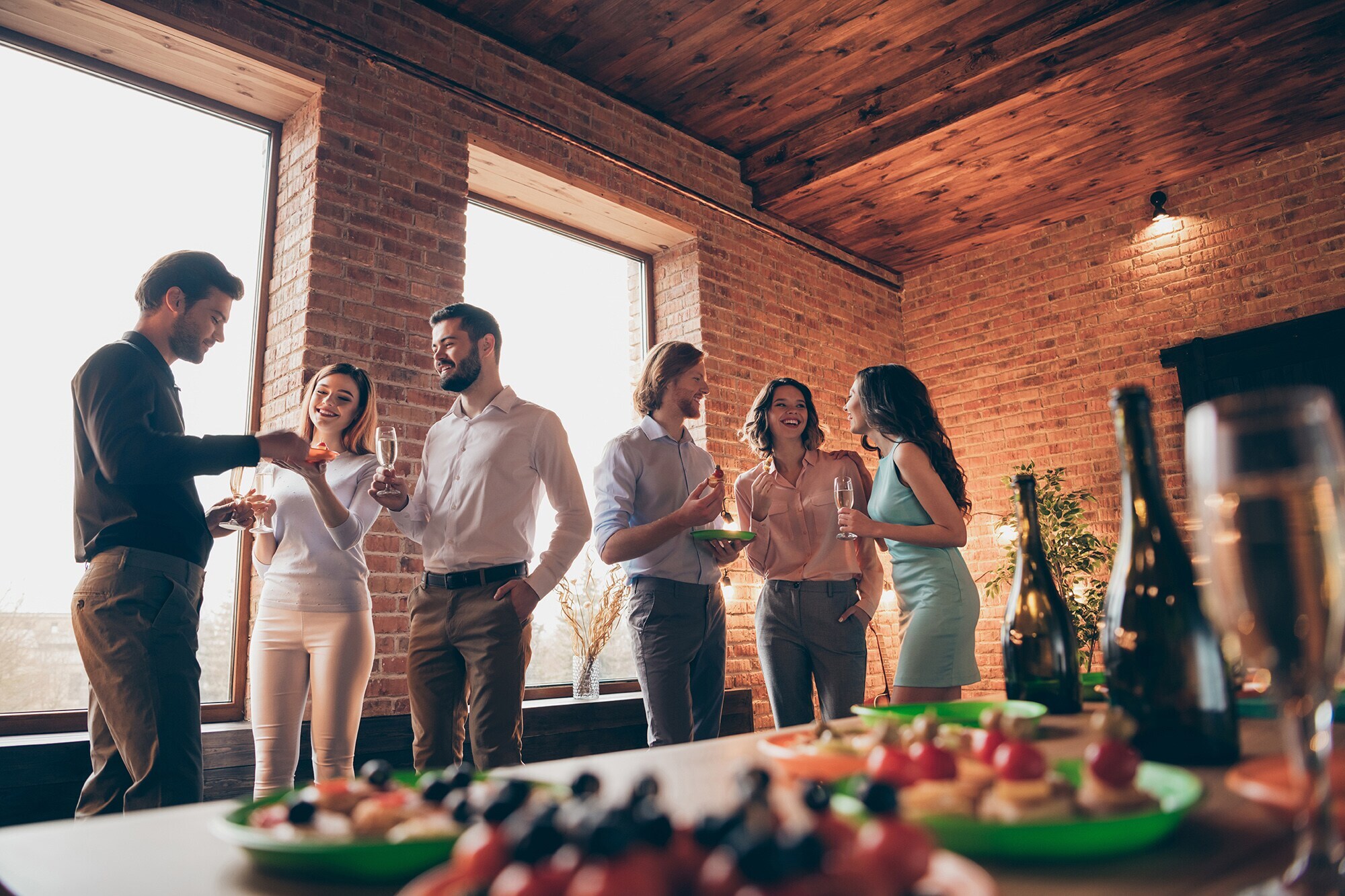 Eine Gruppe von sechs Menschen steht vor einem Fingerfood Buffet mit Sekt.