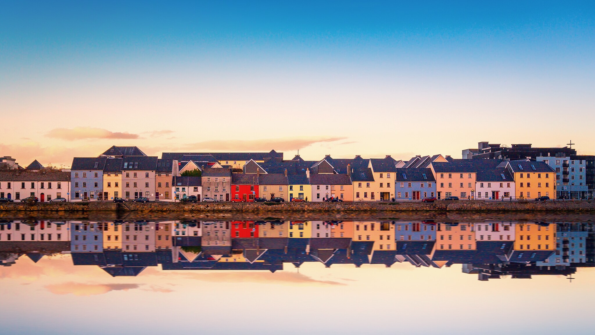 Etliche bunte, kleine Häuser stehen an einem Wasser, die Häuser spiegeln sich in der Wasseroberfläche.