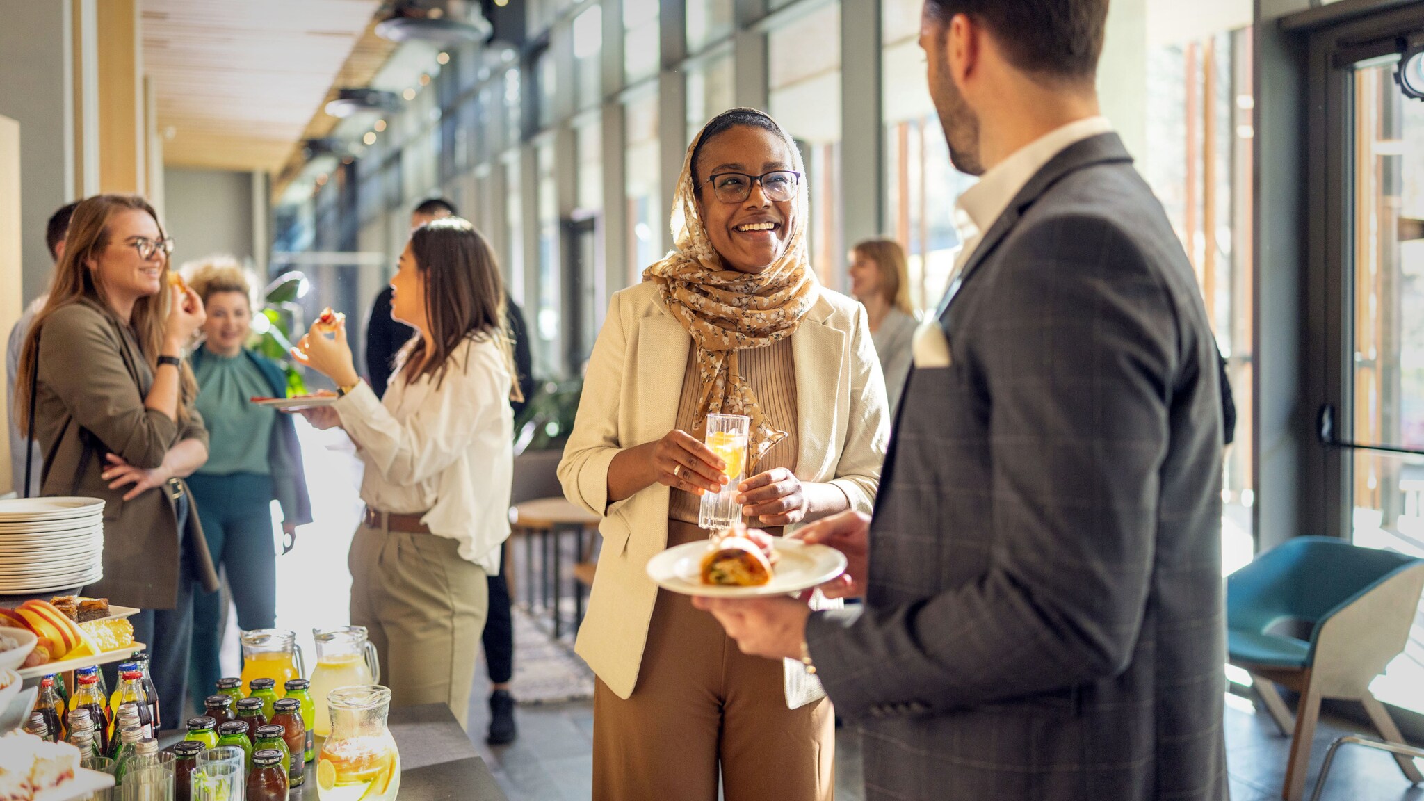Eine Frau und ein Mann unterhalten sich an einem Büfett in einem hellen Foyer, im Hintergrund stehen weitere Personen.
