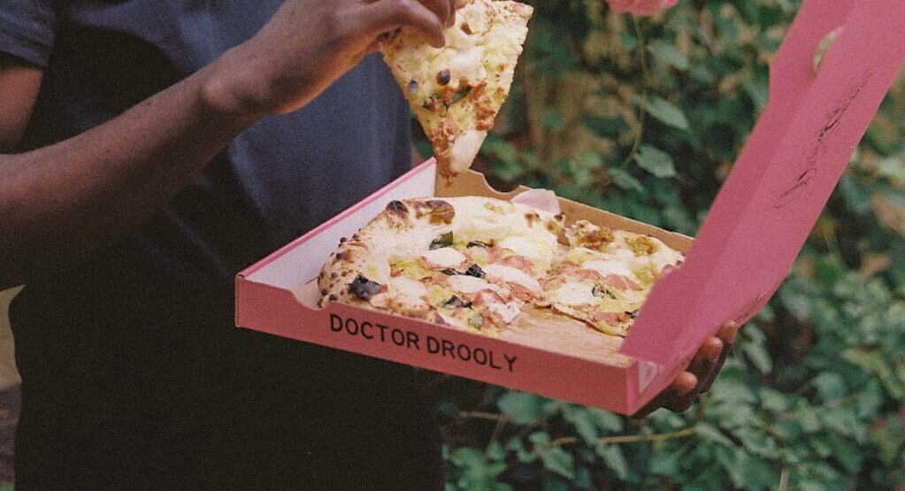 Eine Hand greift ein Stück Pizza aus einer Pizzaschachtel