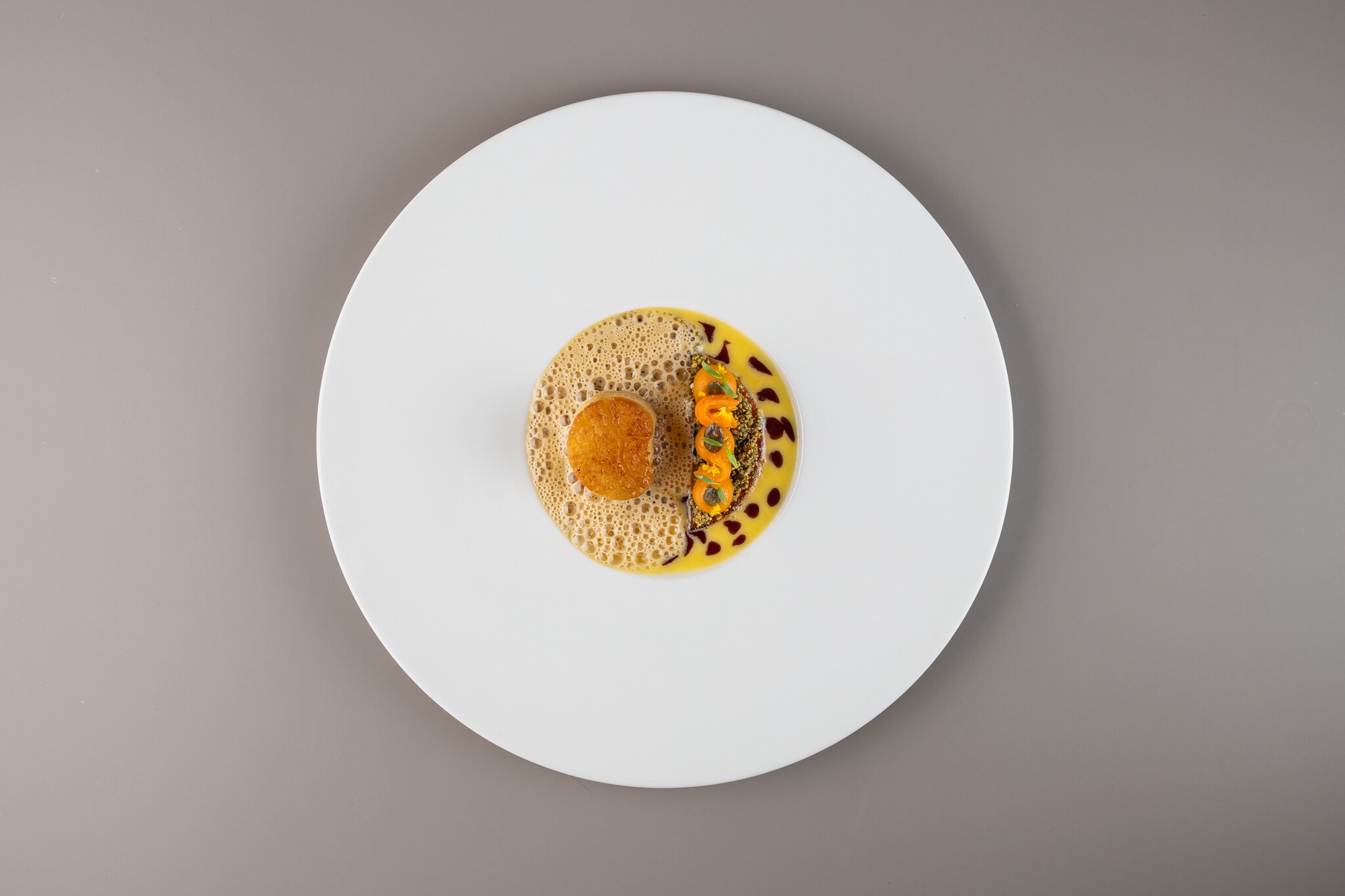 Rundes Gericht mit einer gebackenen Kugel auf Schaum, daneben gelbe Sauce mit kleinen orangefarbenen und schwarzen Tupfen auf weißem Teller, Mount Congreve Estate Gardens, Co Waterford.