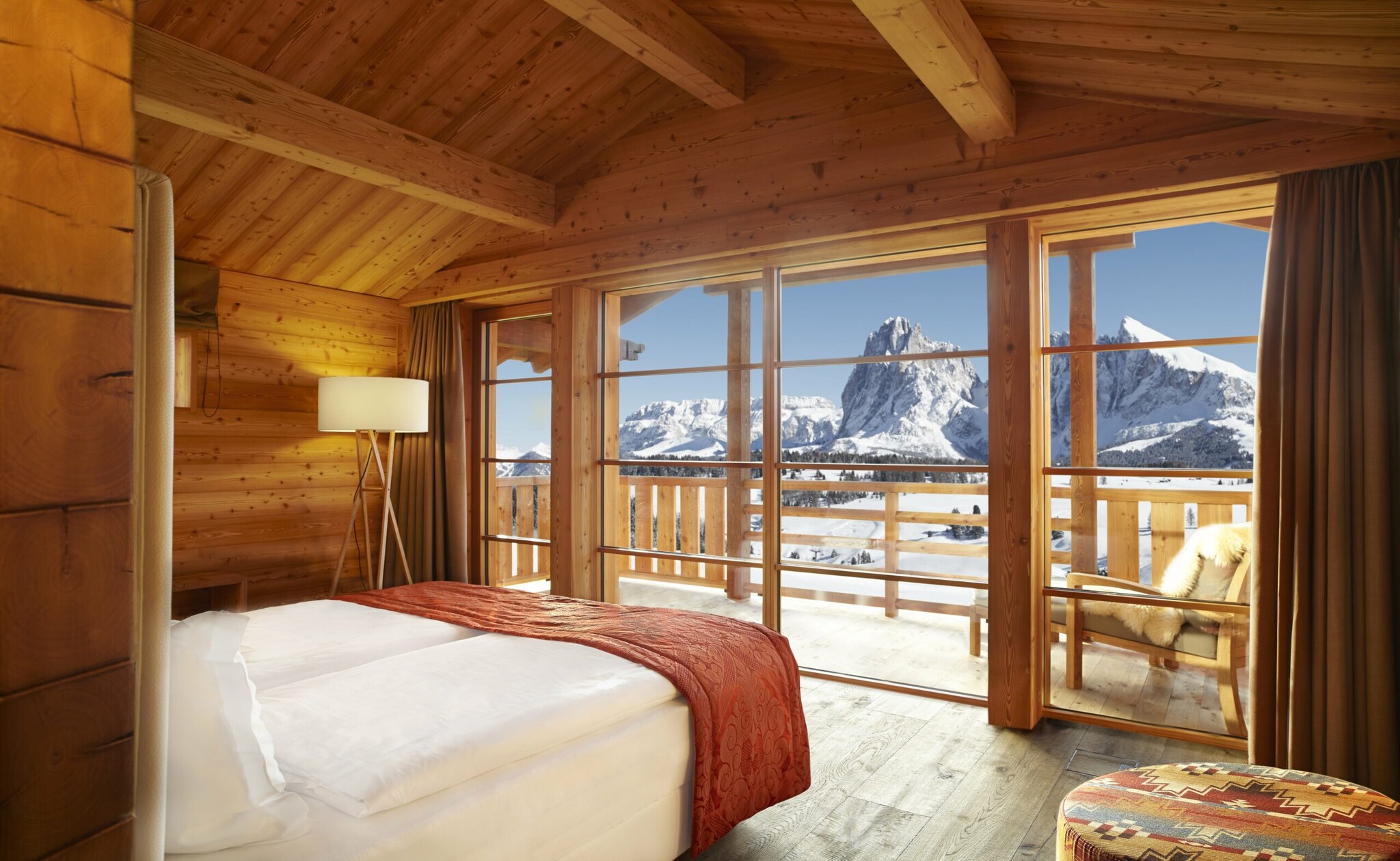 Innenansicht eines Hotelzimmers mit großer Fensterfront, im Hintergrund schneebedeckte Berge