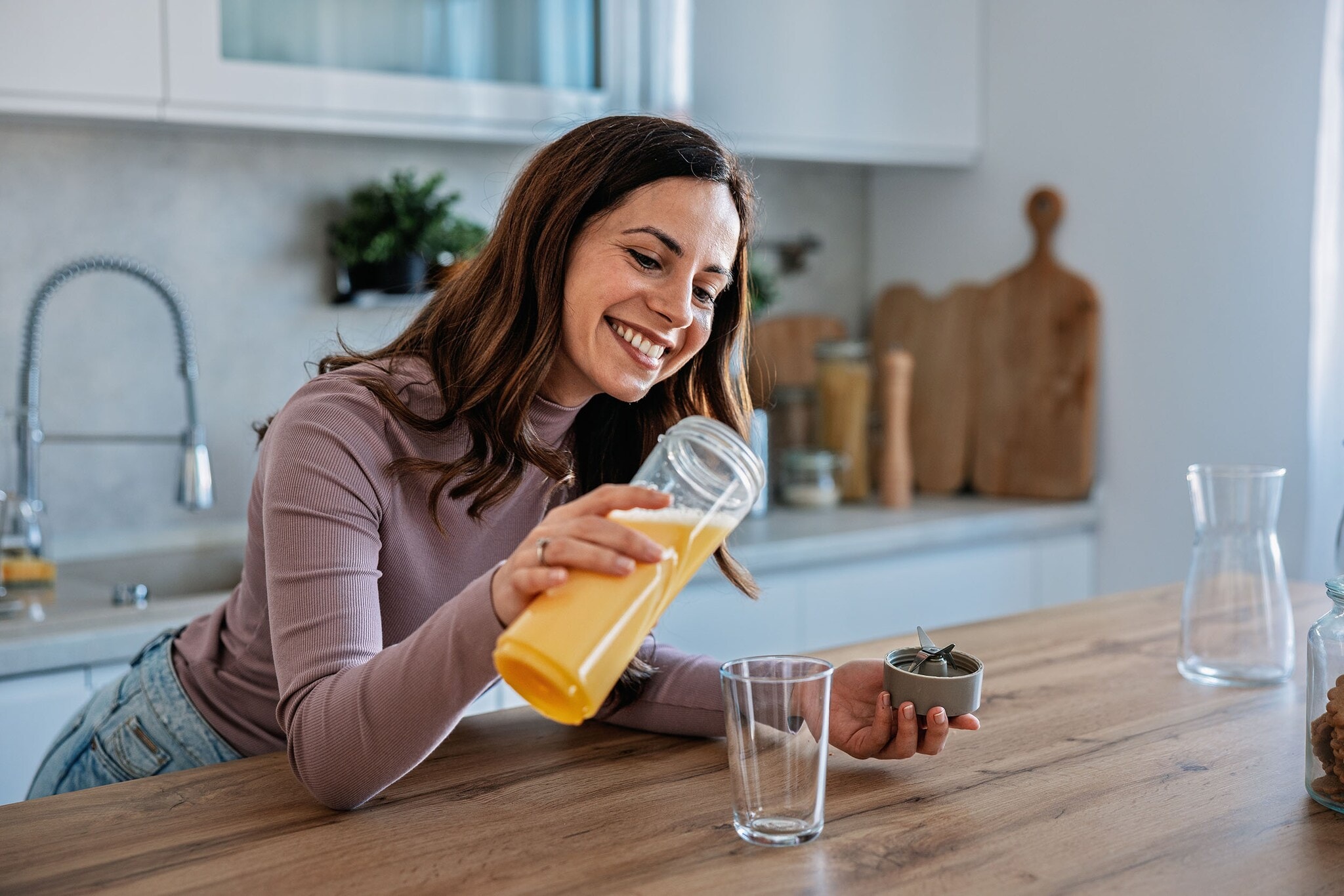 amex-magazin-functional-food-getraenk Eine lächelnde Frau gießt ein gelbes Getränk in eine Glas an einer Küchentheke.