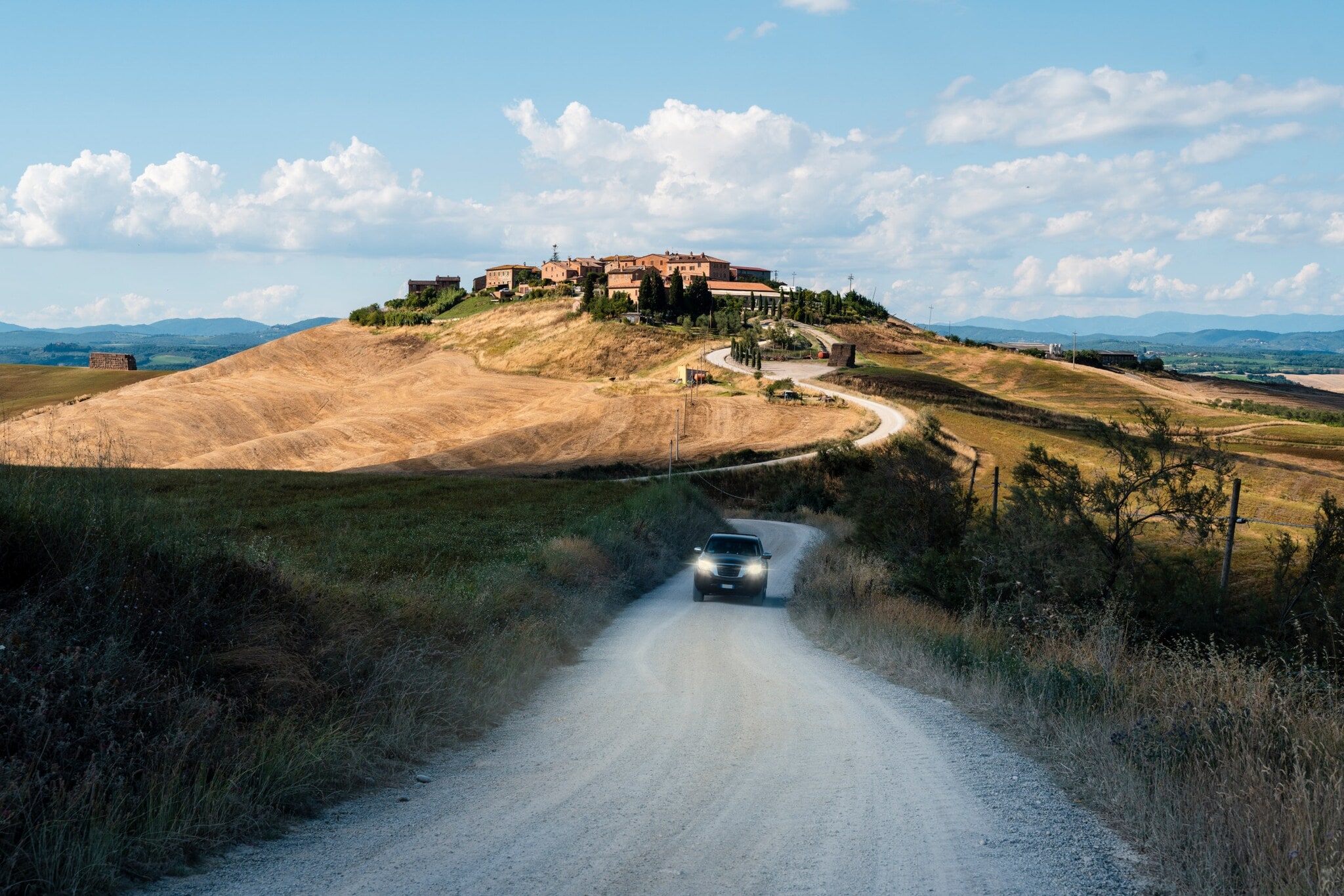 Ein SUV auf einer unbefestigten, kurvigen Straße in mediterraner Landschaft, im Hintergrund eine Ortschaft auf einem Hügel. Ein SUV auf einer unbefestigten, kurvigen Straße in mediterraner Landschaft, im Hintergrund eine Ortschaft auf einem Hügel.