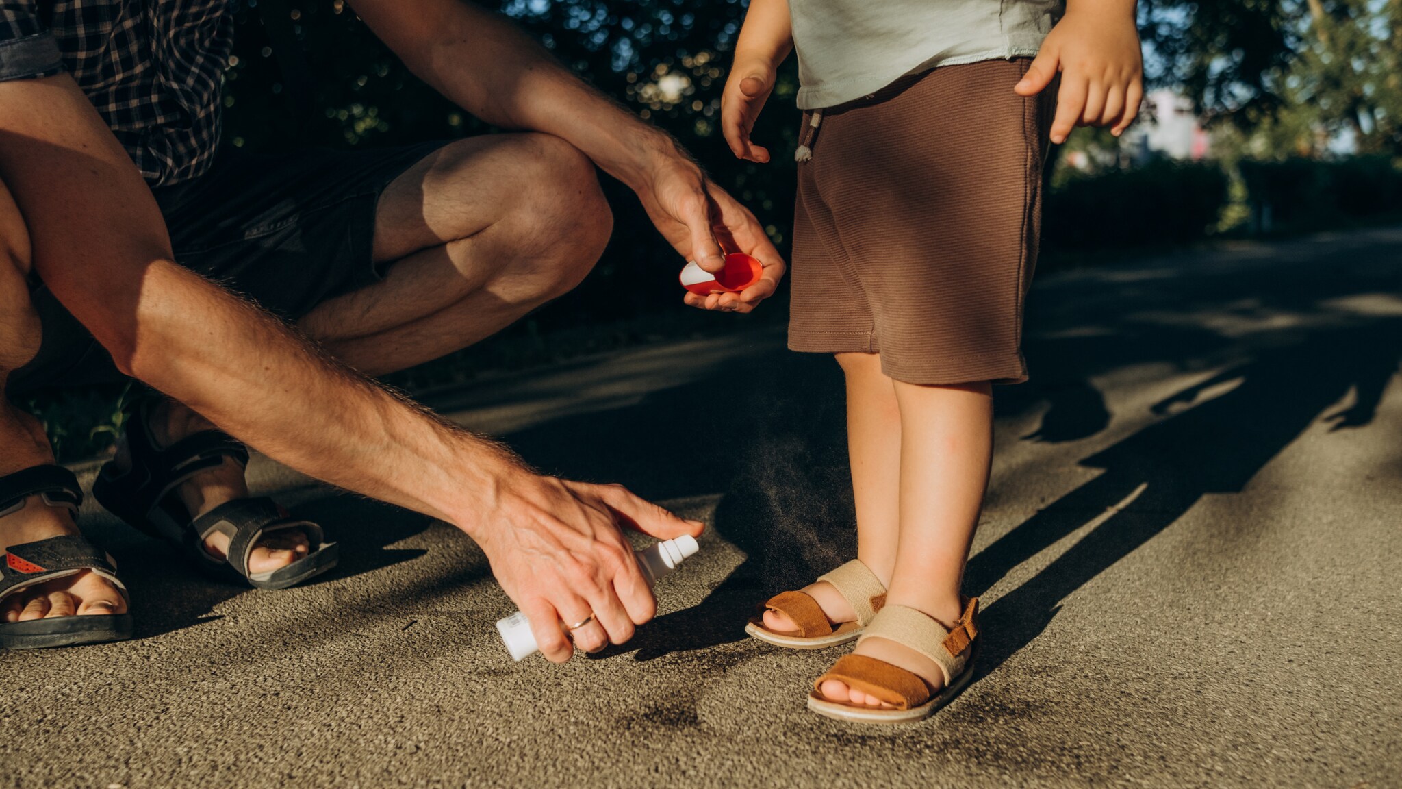 Ein Erwachsener sprüht Insektenspray auf die Füße eines Kindes.