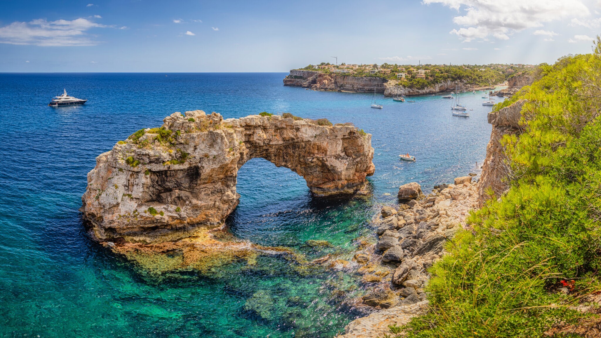Natürlicher Felsenbogen über klarem blauem Meerwasser an der Küste mit mehreren Booten und bewachsenen Klippen