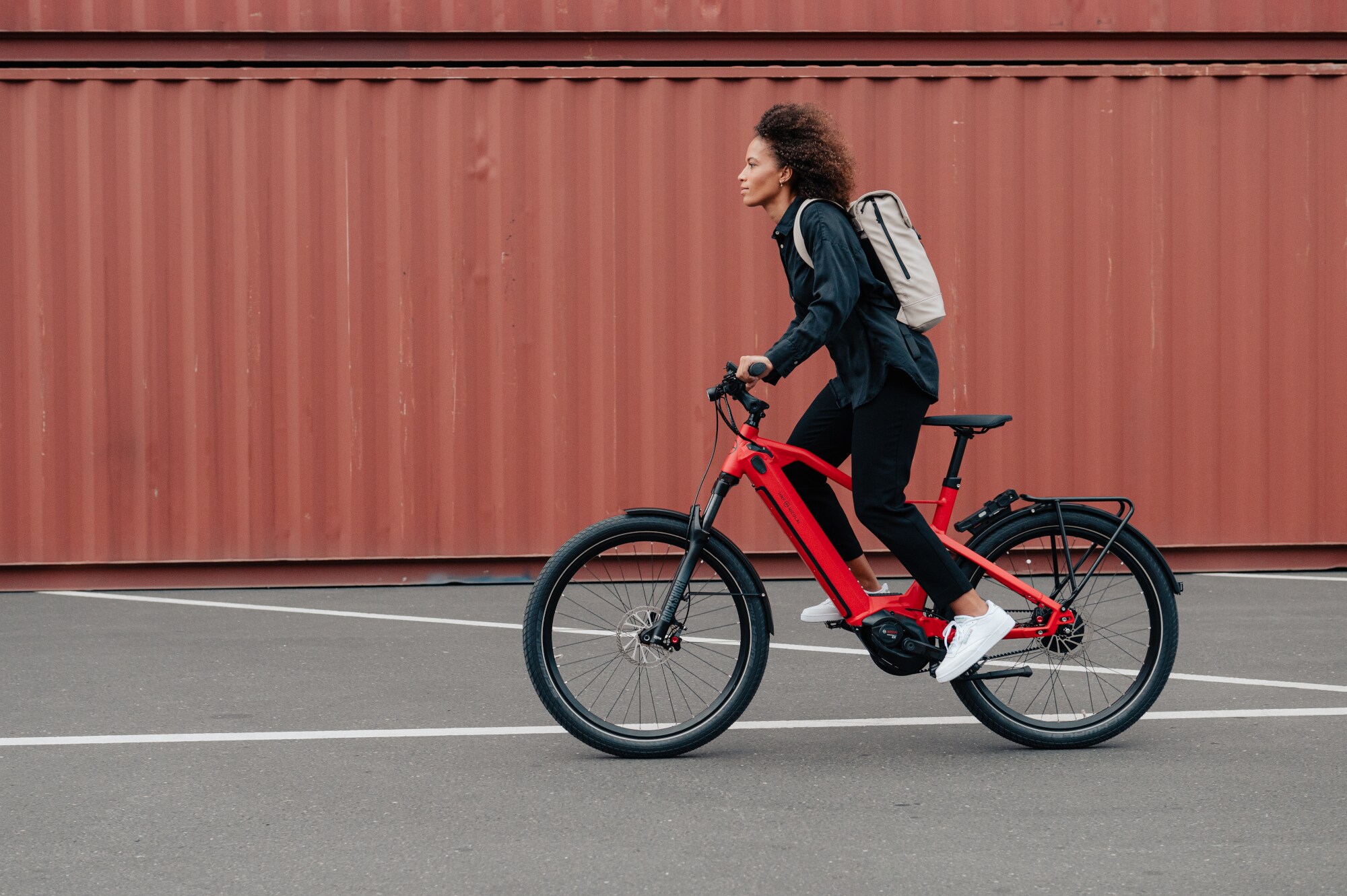 Eine Frau fährt auf einem roten E-Bike vor einem braunen Container