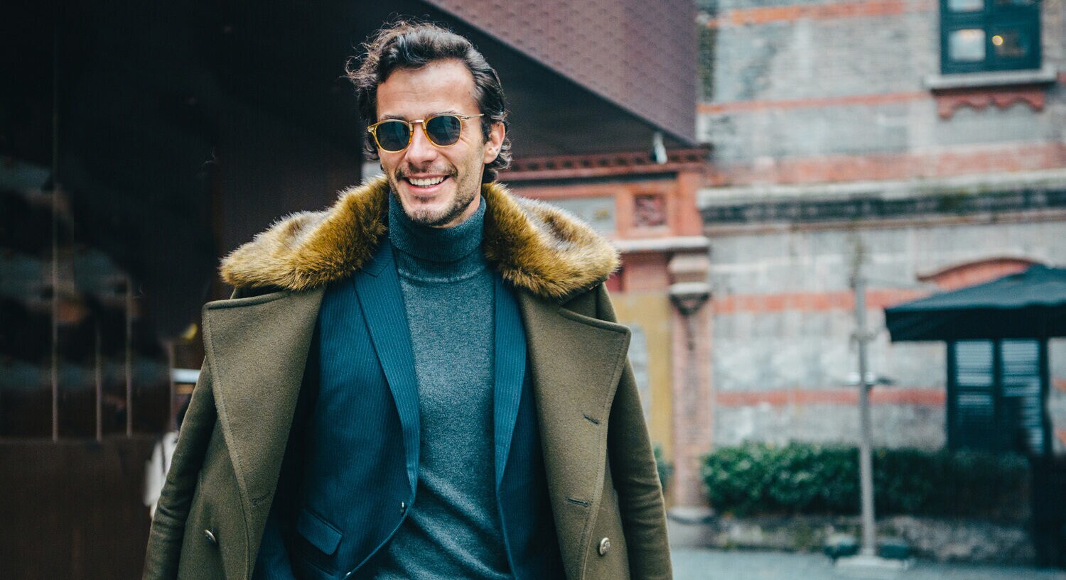 Ein Mann in Anzug und Mantel trägt eine farblich passende Sonnenbrille