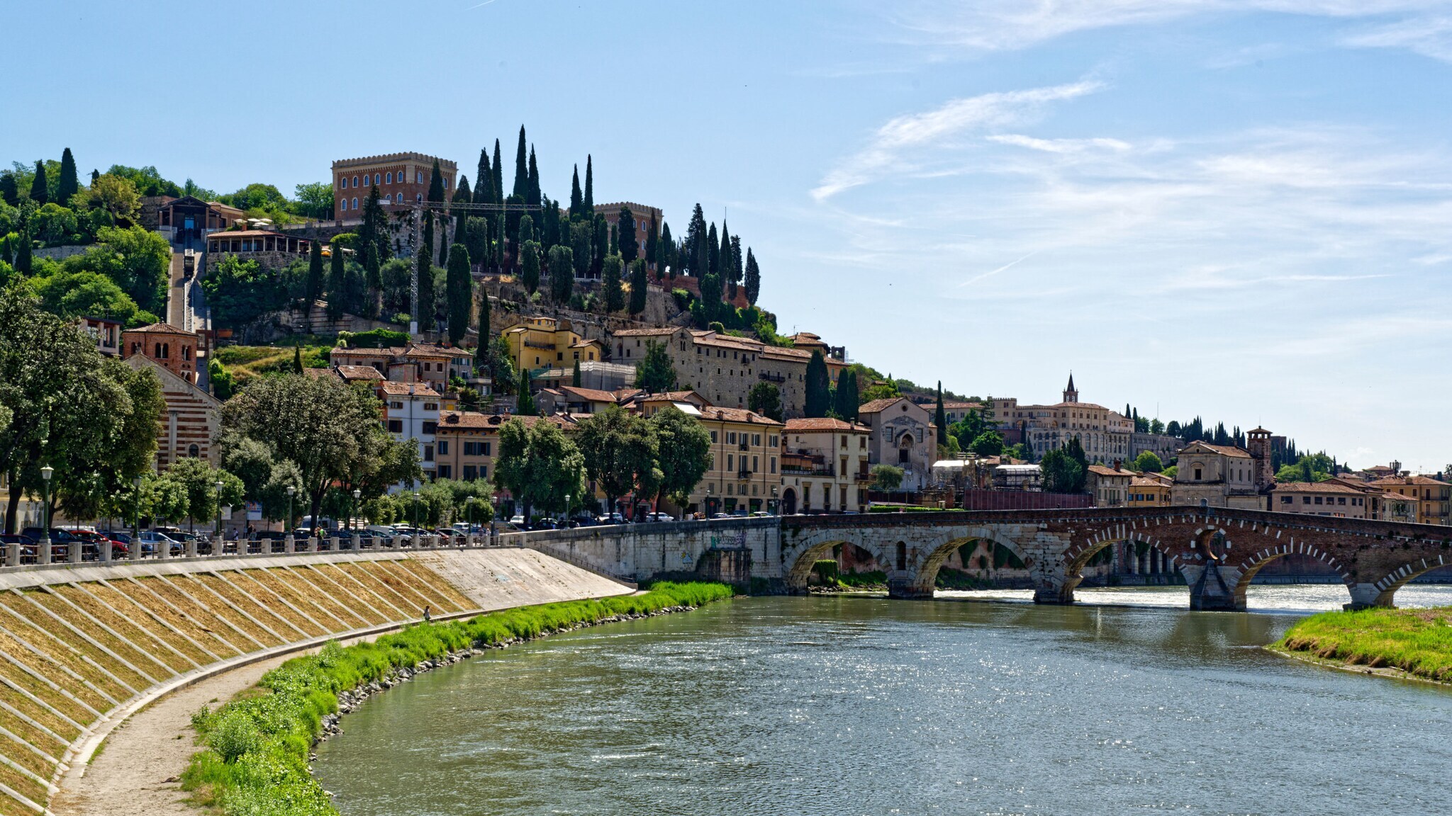 Italienische Stadt auf einem Hügel mit Zypressen an einem Fluss mit Bogensteinbrücke.