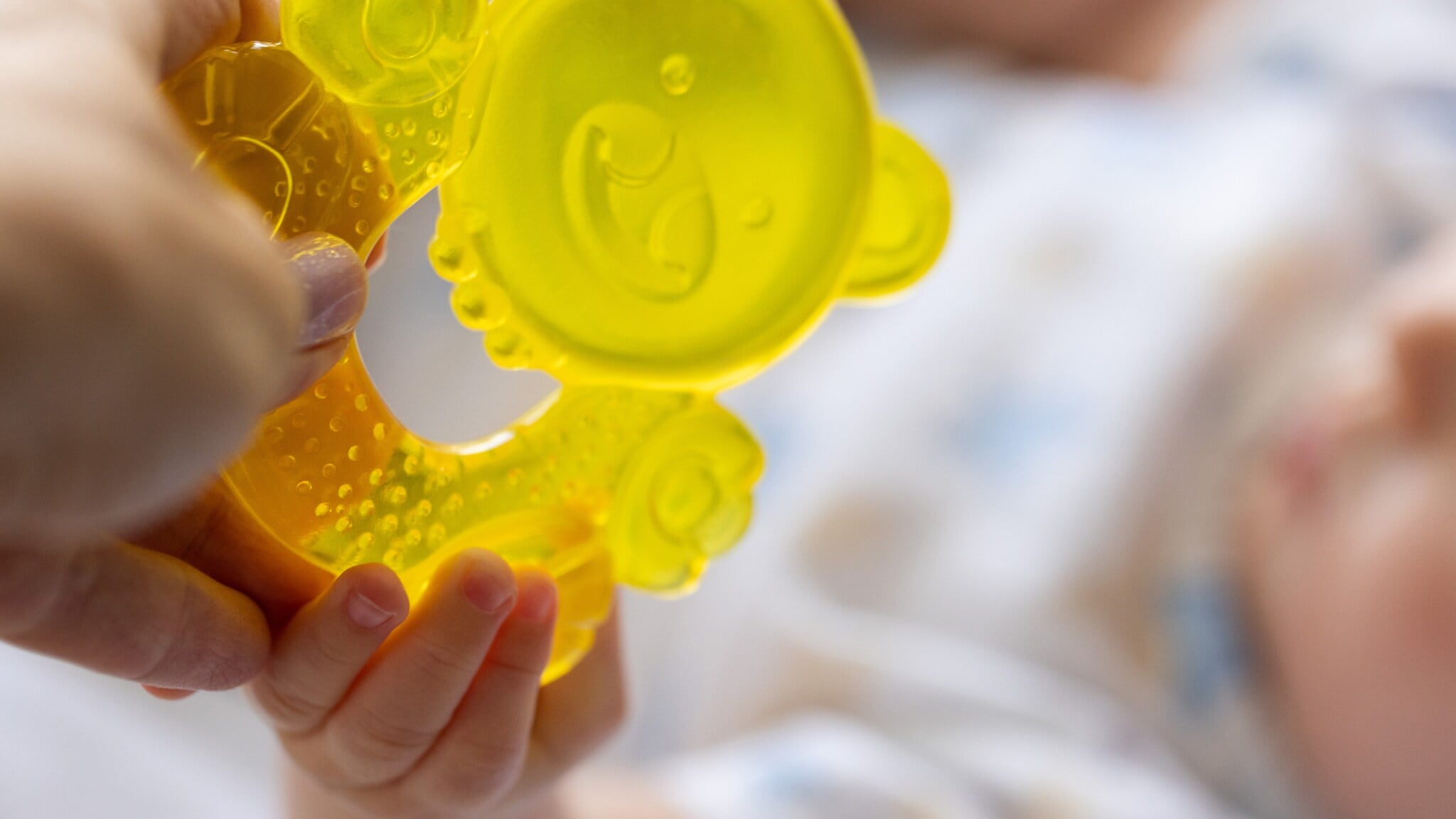 Hand hält gelbes, transparentes Baby-Beißspielzeug, das von einem Baby mit kleinen Fingern gehalten wird. Hand hält gelbes, transparentes Baby-Beißspielzeug, das von einem Baby mit kleinen Fingern gehalten wird.