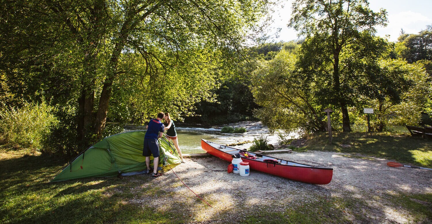 Ein Paar errichtet neben einem Kanu ein Zelt an der Altmühl.