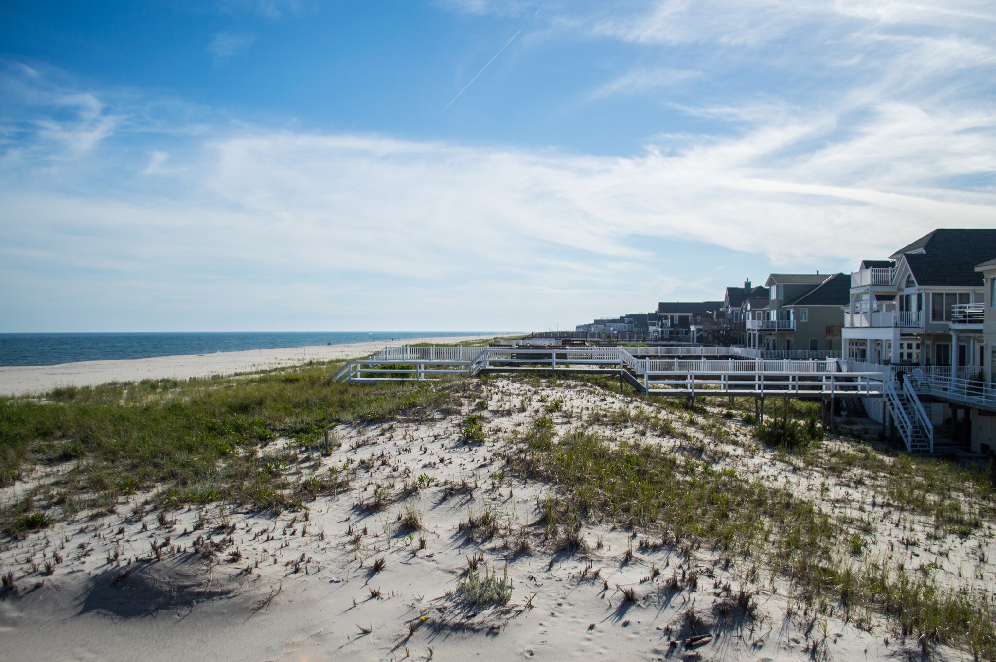 Weg zu einem Sandstrand mit Dünen unter blauem Himmel.