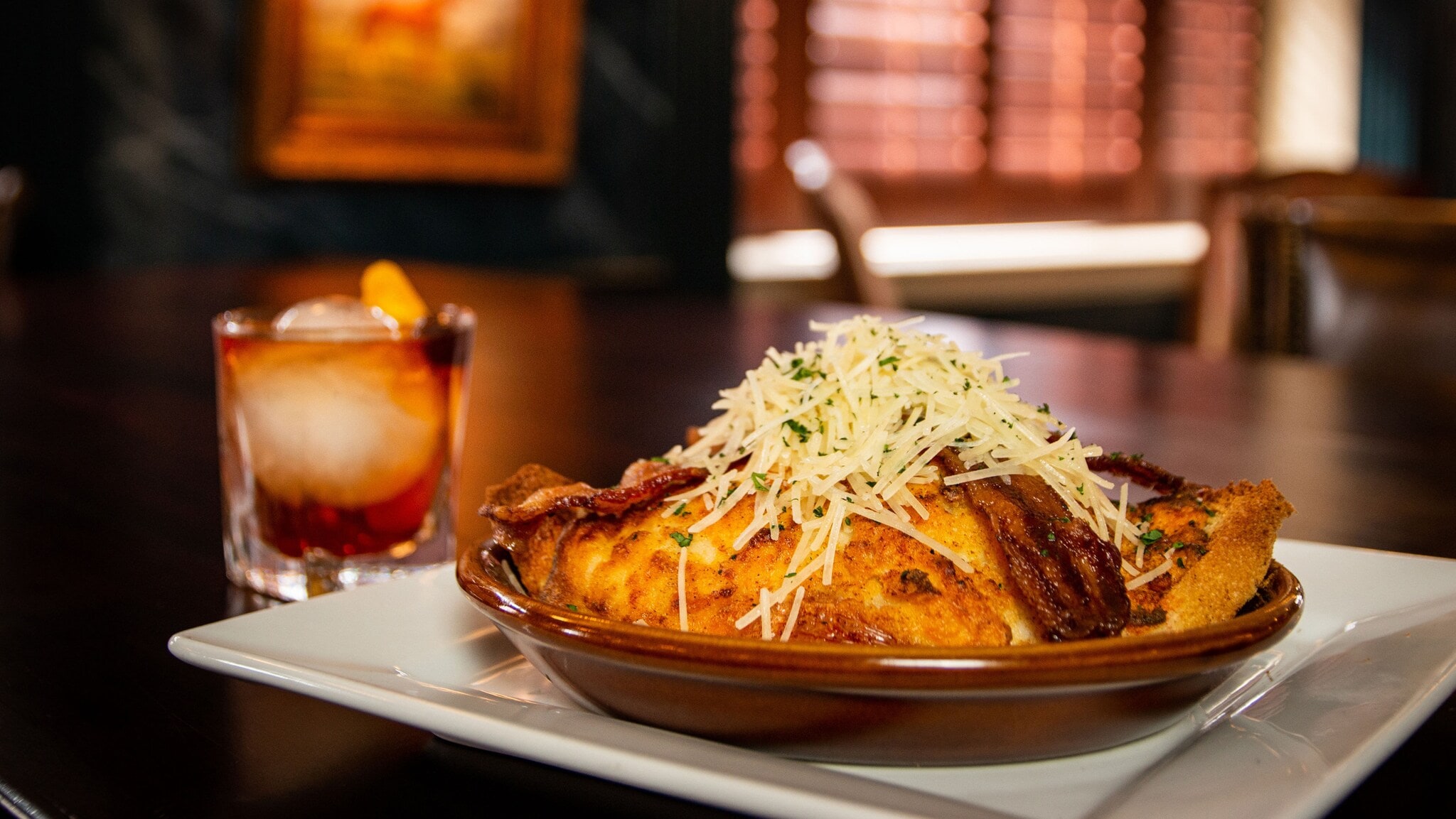 Hot Brown Sandwich mit Schinken, Speck und Käse auf braunem Teller, daneben ein Old Fashioned Cocktail mit Orangenscheibe Hot Brown Sandwich mit Schinken, Speck und Käse auf braunem Teller, daneben ein Old Fashioned Cocktail mit Orangenscheibe