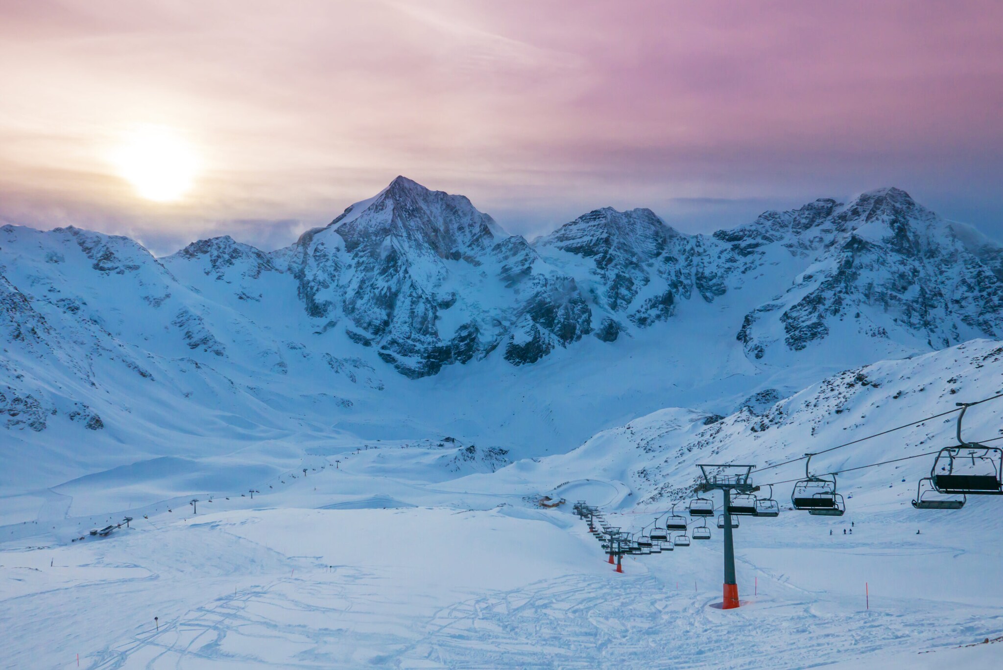 Leeres Skigebiet mit Sessellift vor Bergmassiv bei Sonnenaufgang