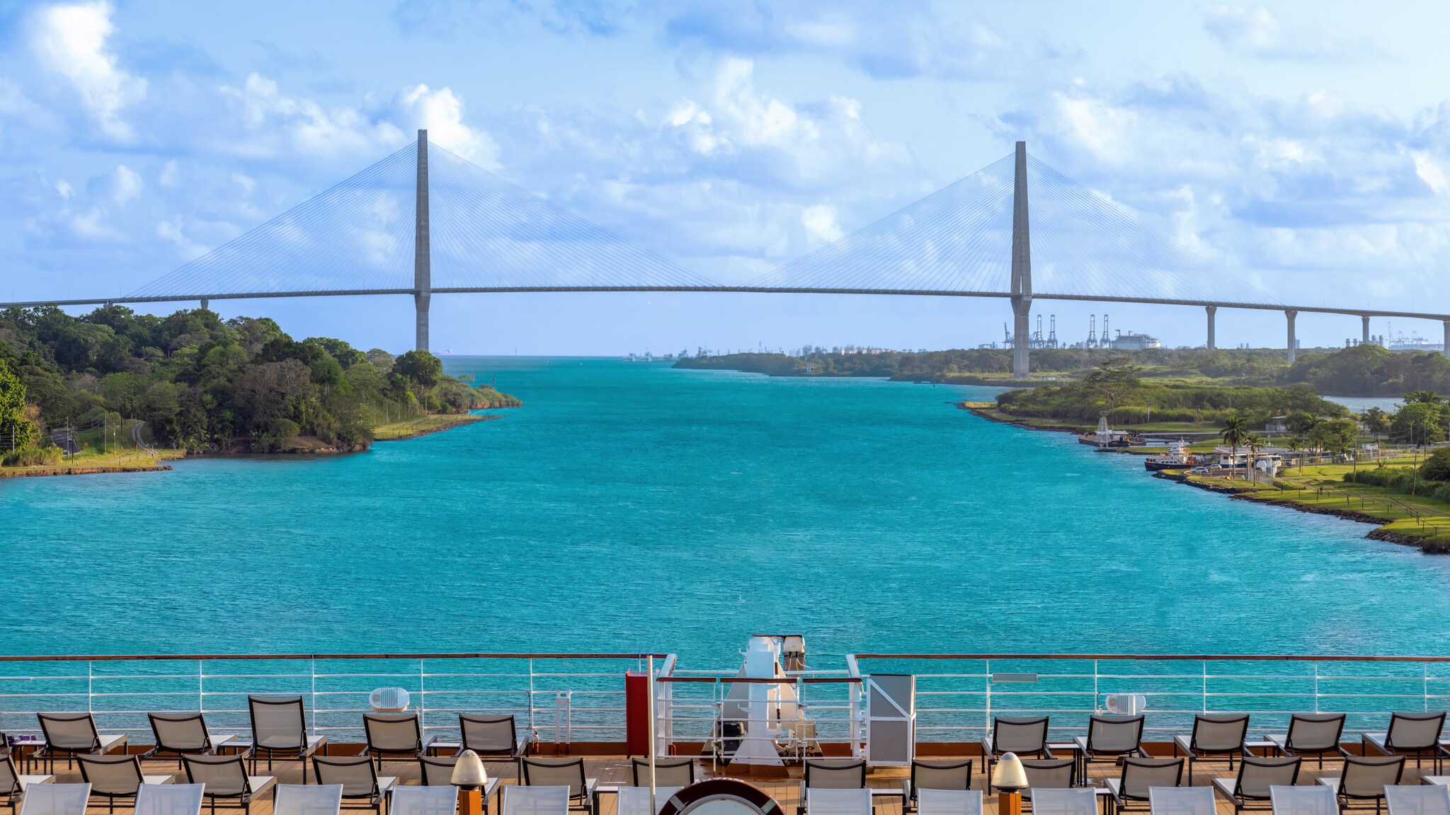 Blick auf eine lange Schrägkabelbrücke über einer Wasserstraße von einem Schiff aus, im Vordergrund Stuhlreihen an Deck. Blick auf eine lange Schrägkabelbrücke über einer Wasserstraße von einem Schiff aus, im Vordergrund Stuhlreihen an Deck.
